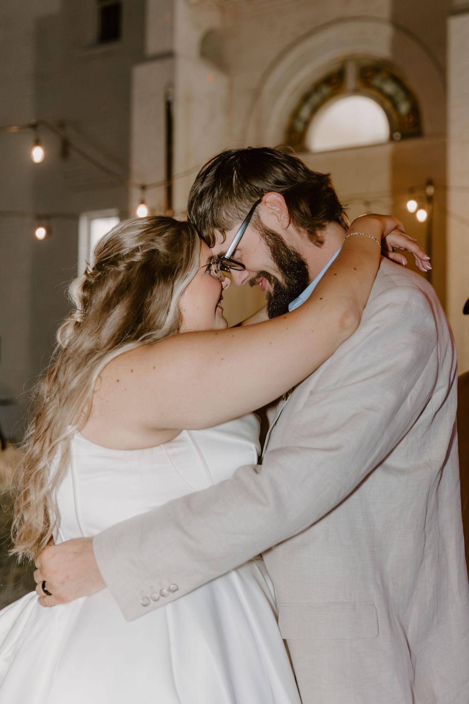 A tender moment captured between a couple in white and grey attire during an indoor wedding celebration.