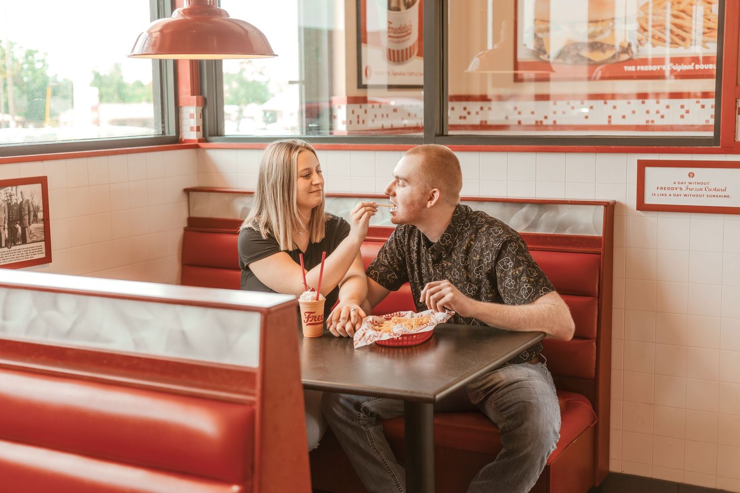 Couple sharing meal and conversation in retro-style diner with red booth seating.