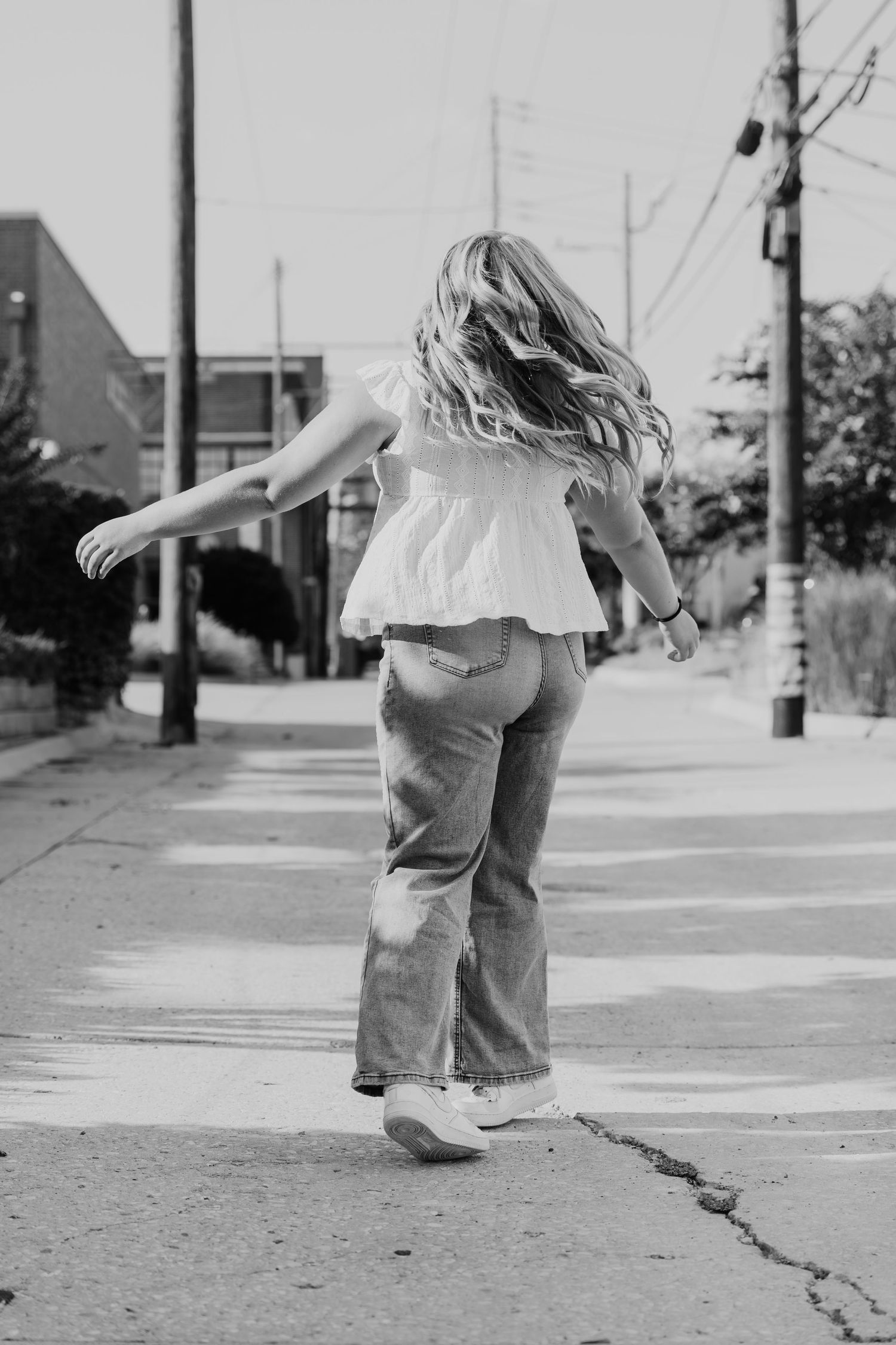 Black and white photo of someone twirling on a sidewalk wearing a flowy white top and jeans on a summer day.