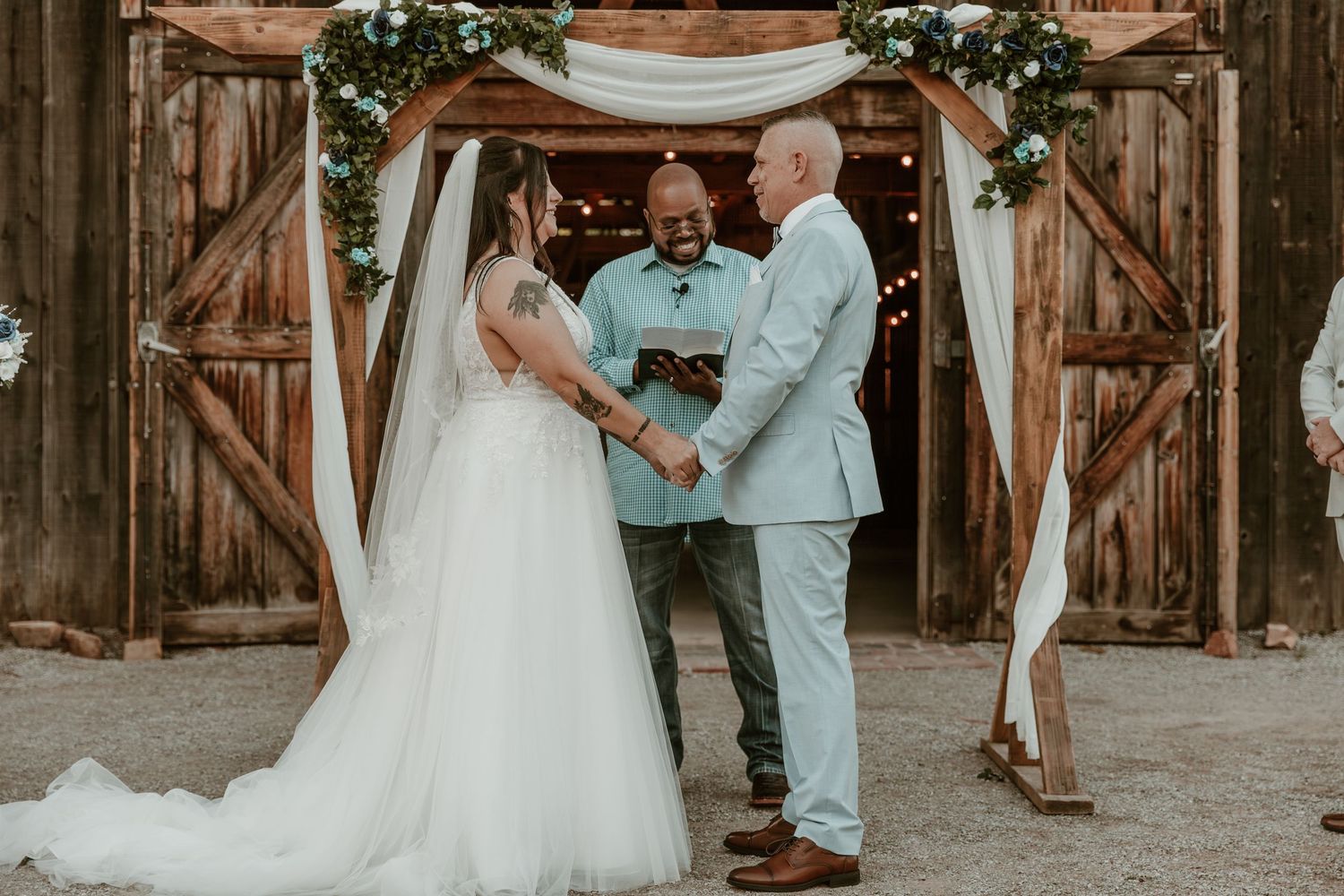A rustic barn wedding ceremony with white draping and greenery arch during an intimate celebration.