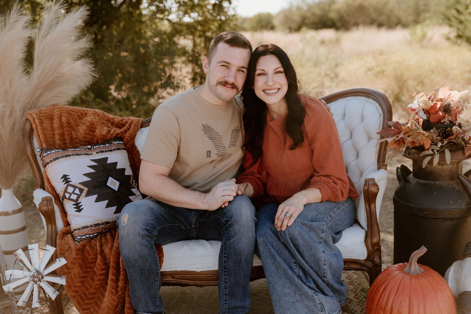 Couple sitting on vintage sofa in outdoor autumn setting with pumpkins and fall decor.
