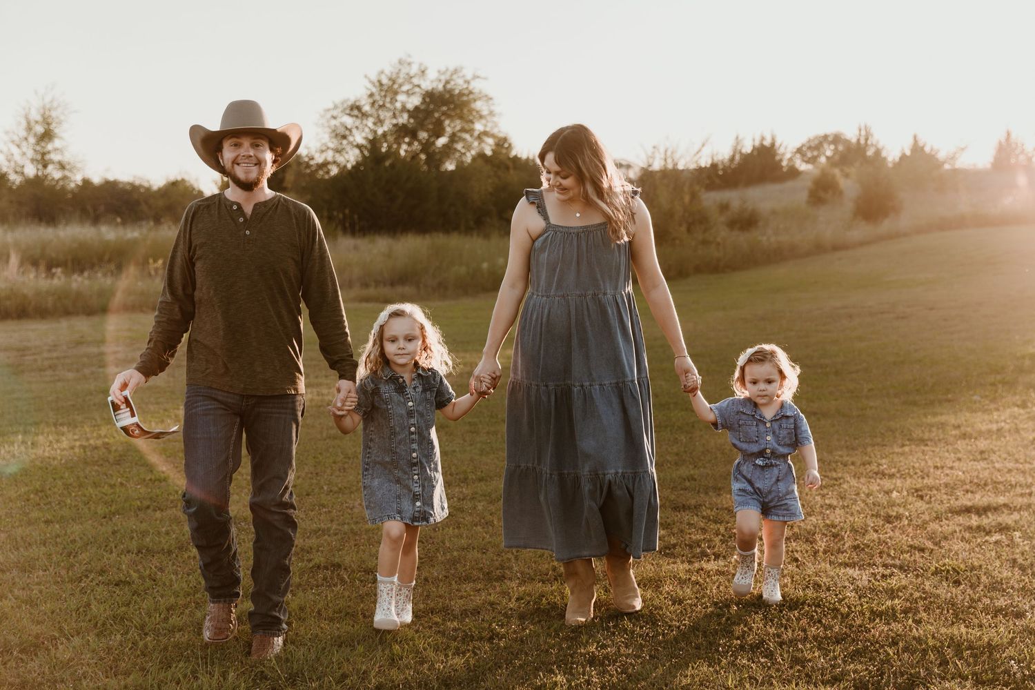 A family walks together through a golden field at sunset, creating silhouettes against the warm glowing sky.