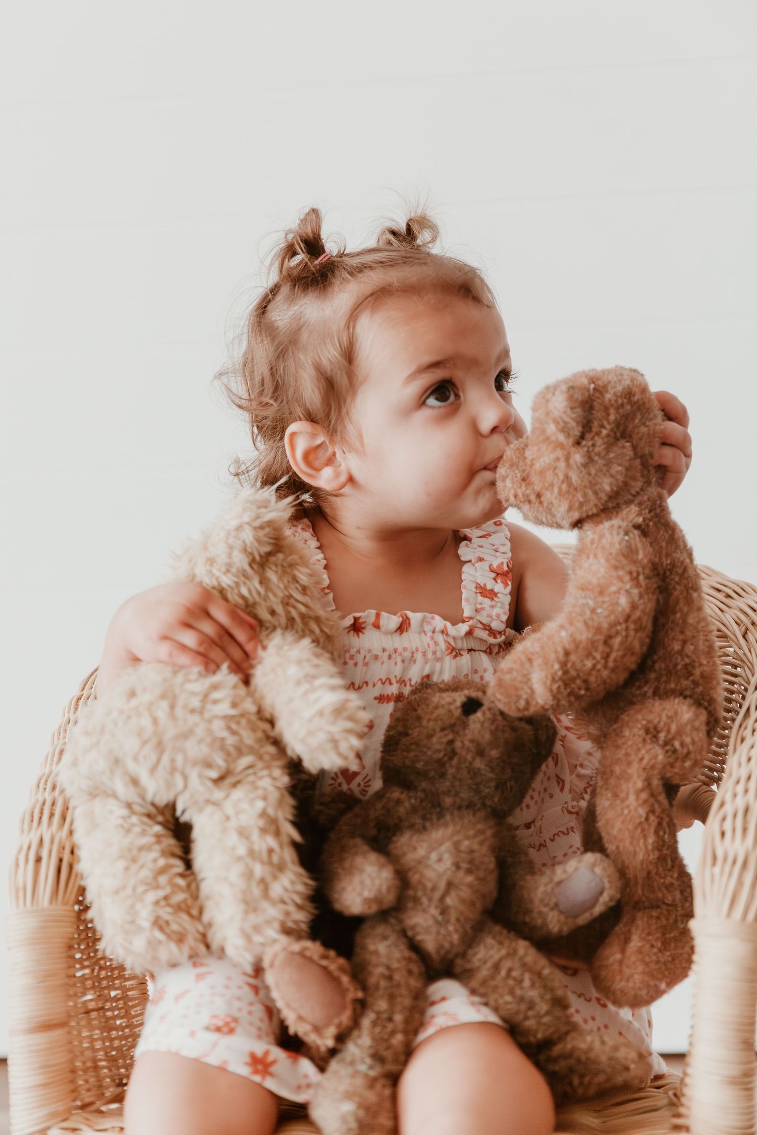 A sweet moment between a toddler and their favorite teddy bear, sharing multiple playful kisses against a soft neutral background.
