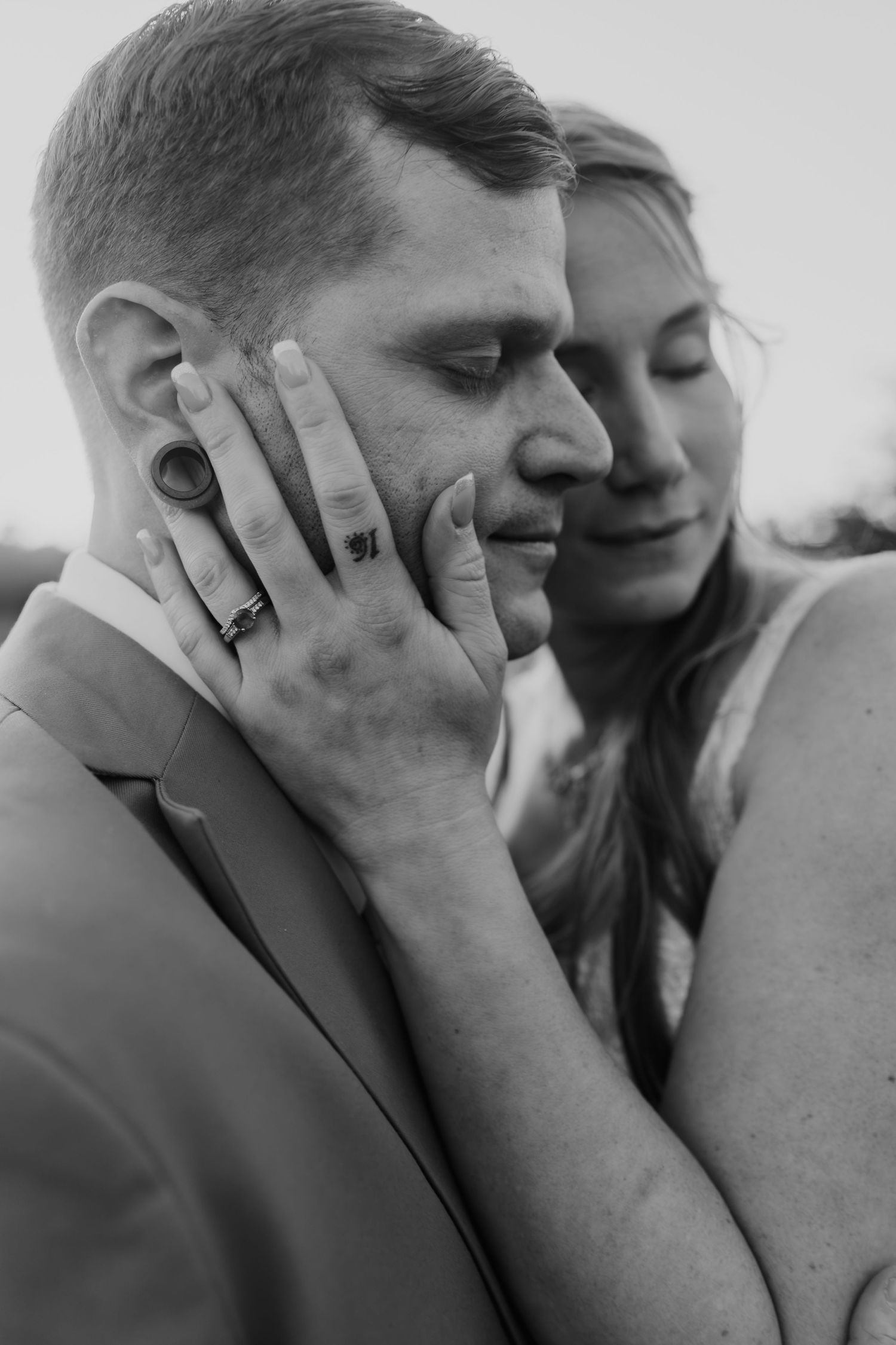 Black and white wedding photo of groom with closed eyes as bride tenderly cups his face, both wearing rings.