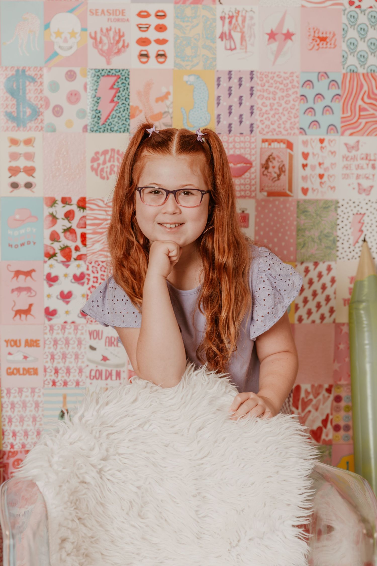 A person leans on a white furry chair against a pastel patterned wallpaper background in a studio setting.