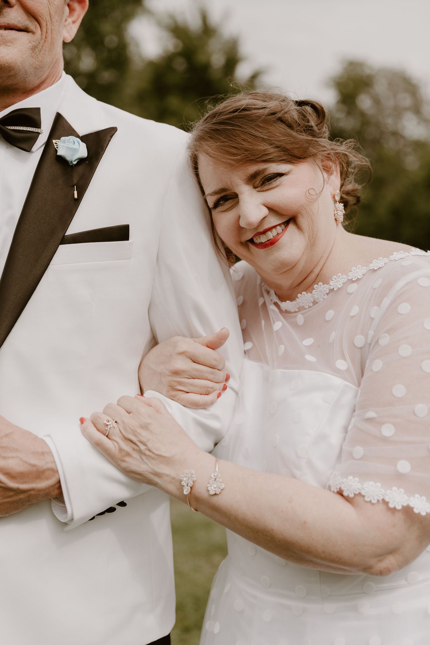 A romantic closeup of a couple in wedding attire laughing and embracing during their outdoor photoshoot.