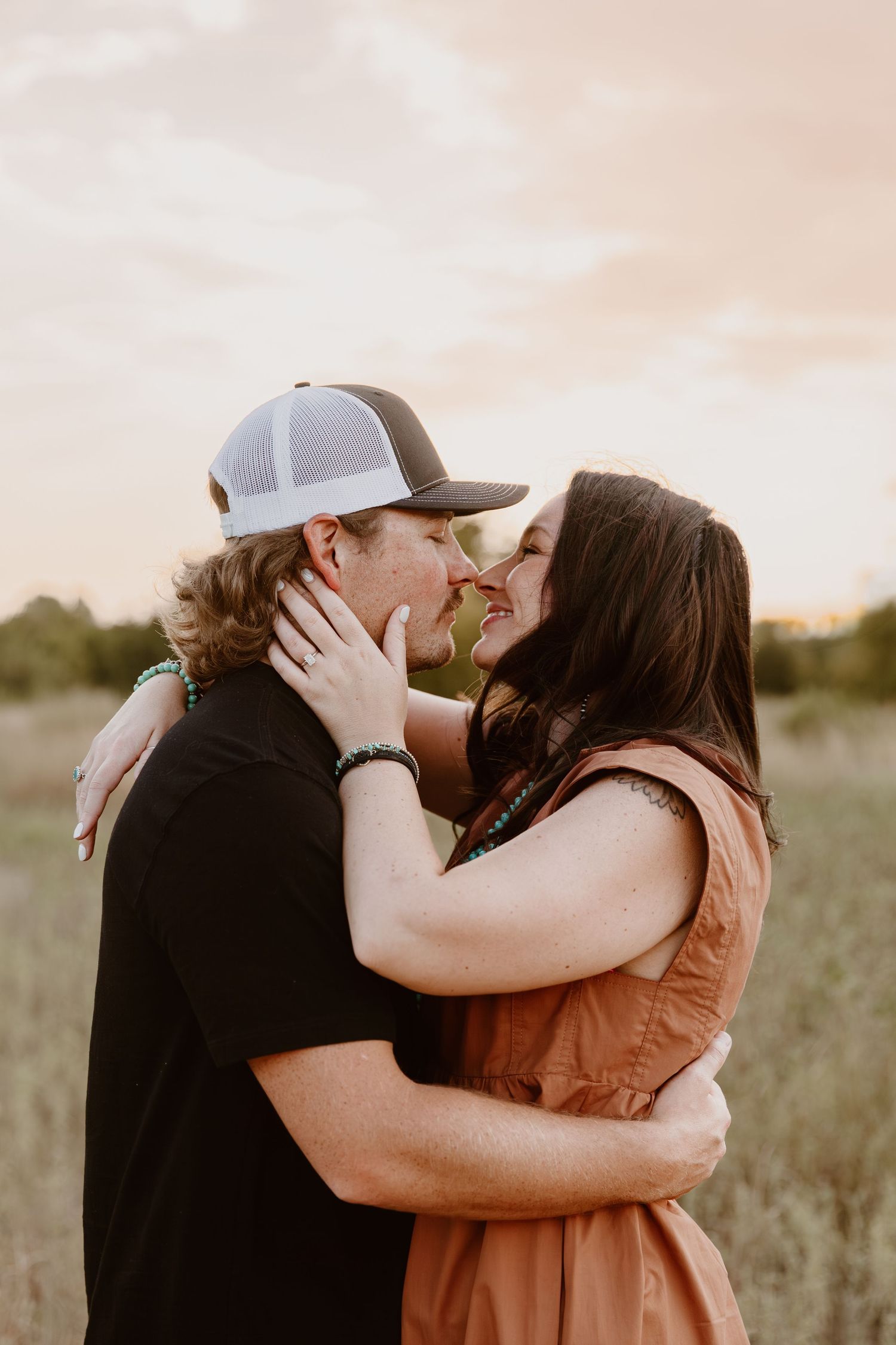 Four romantic photos of a couple in a field at sunset sharing tender embraces and kisses.