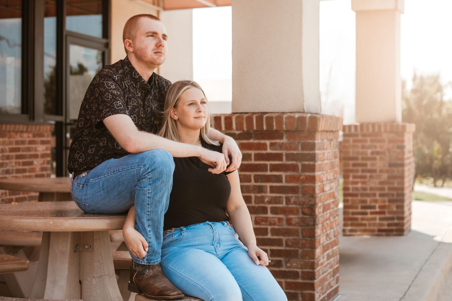 A couple sits together on a brick porch bench during a romantic outdoor photo session.
