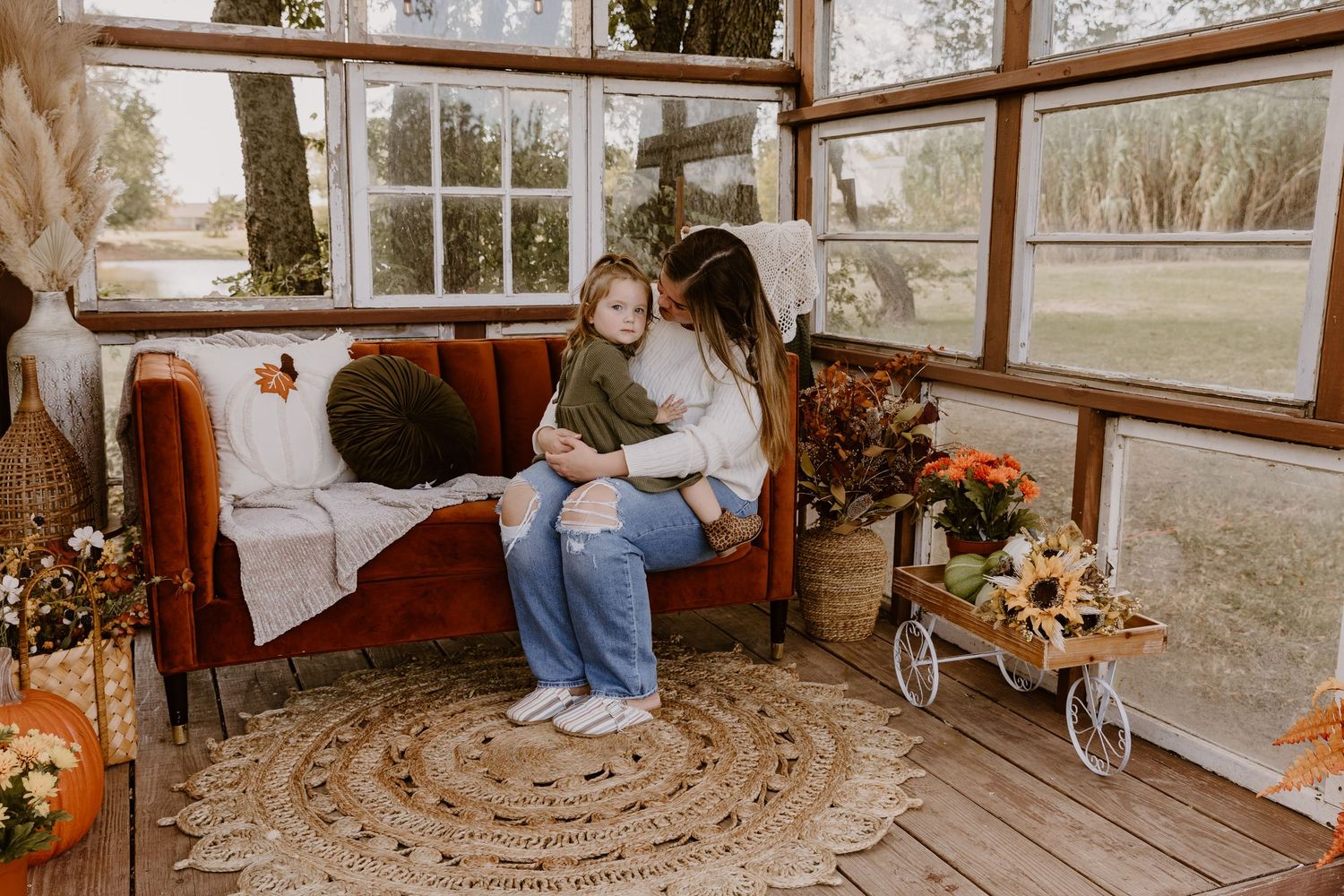 A cozy autumn scene with pumpkins and fall decor arranged on a sunlit porch with windows.