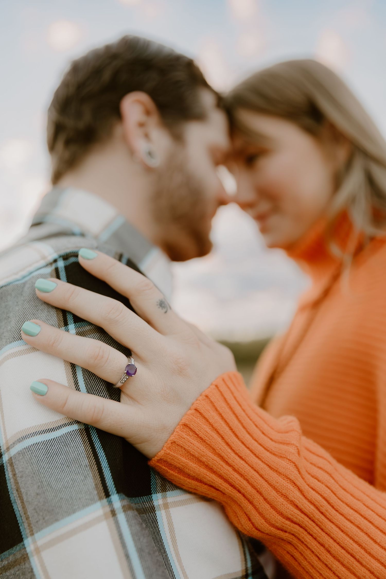 Hand wearing mint green nail polish and a ring holds a book while wearing an orange sweater in soft focus.
