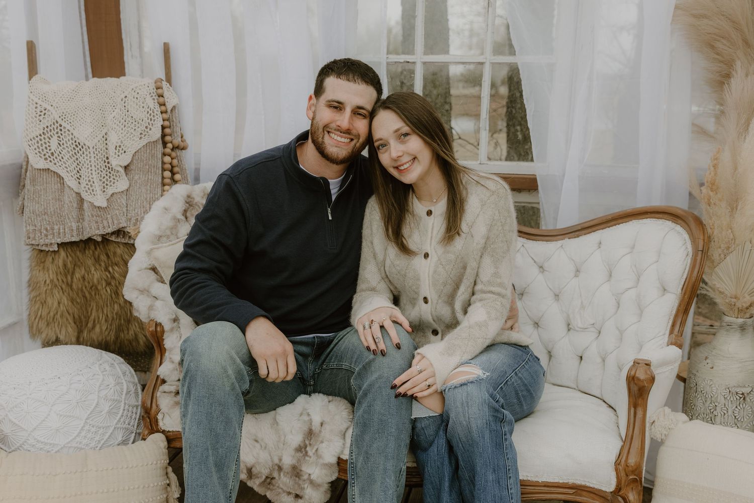 A couple sits close together on a light colored couch in a bright indoor setting.