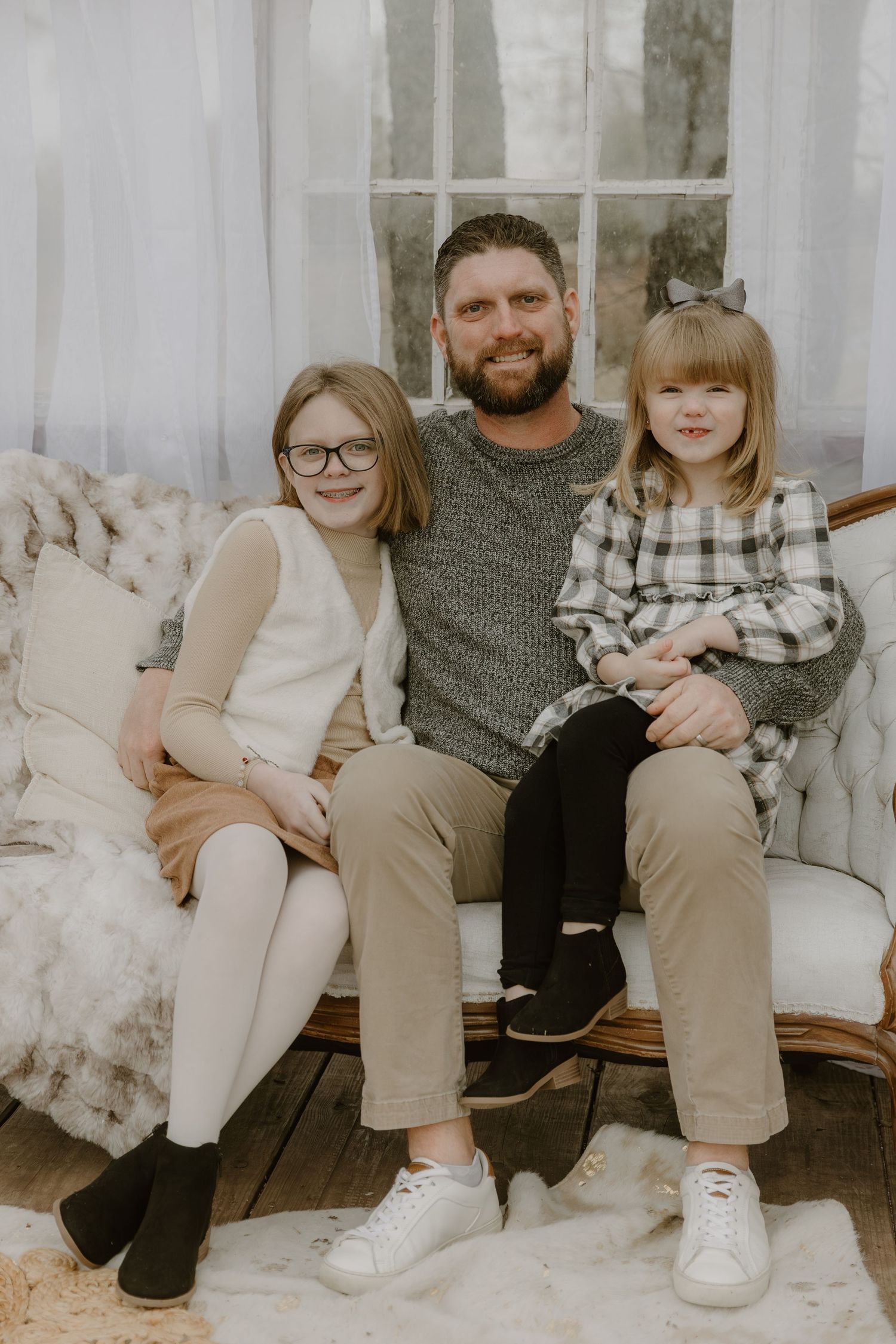 A family sits together on a couch in coordinated neutral-toned outfits for a casual portrait session.