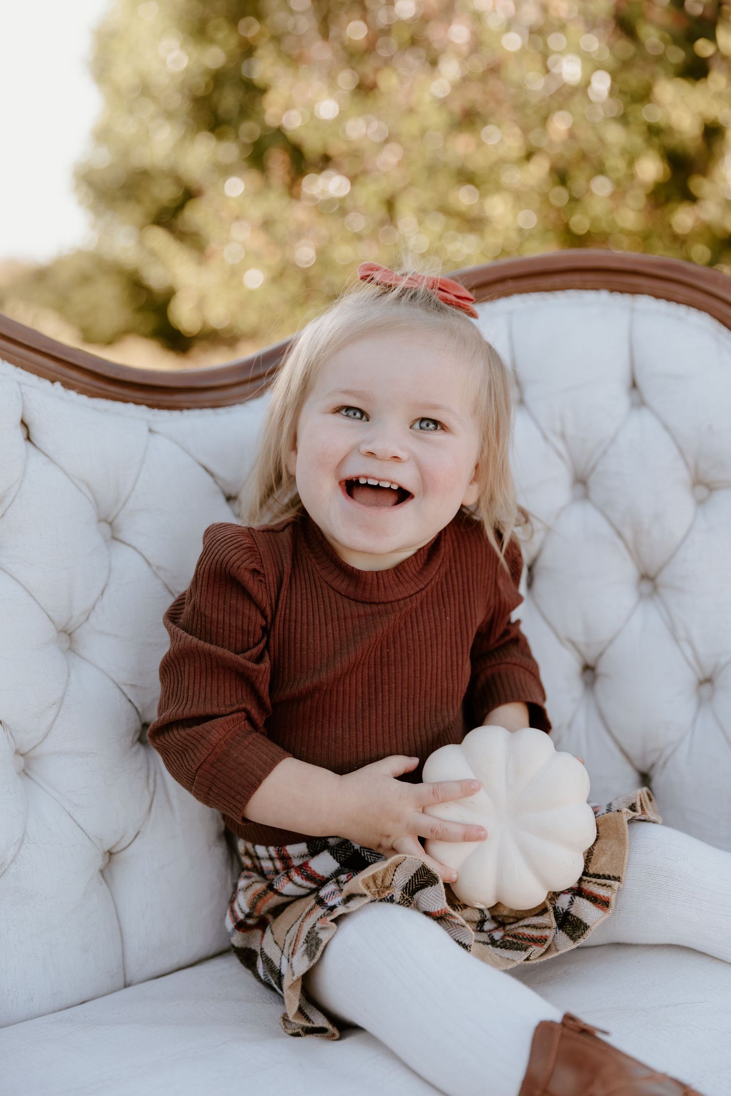 A series of five photos showing a small child in a brown sweater sitting and laughing on a white tufted couch.