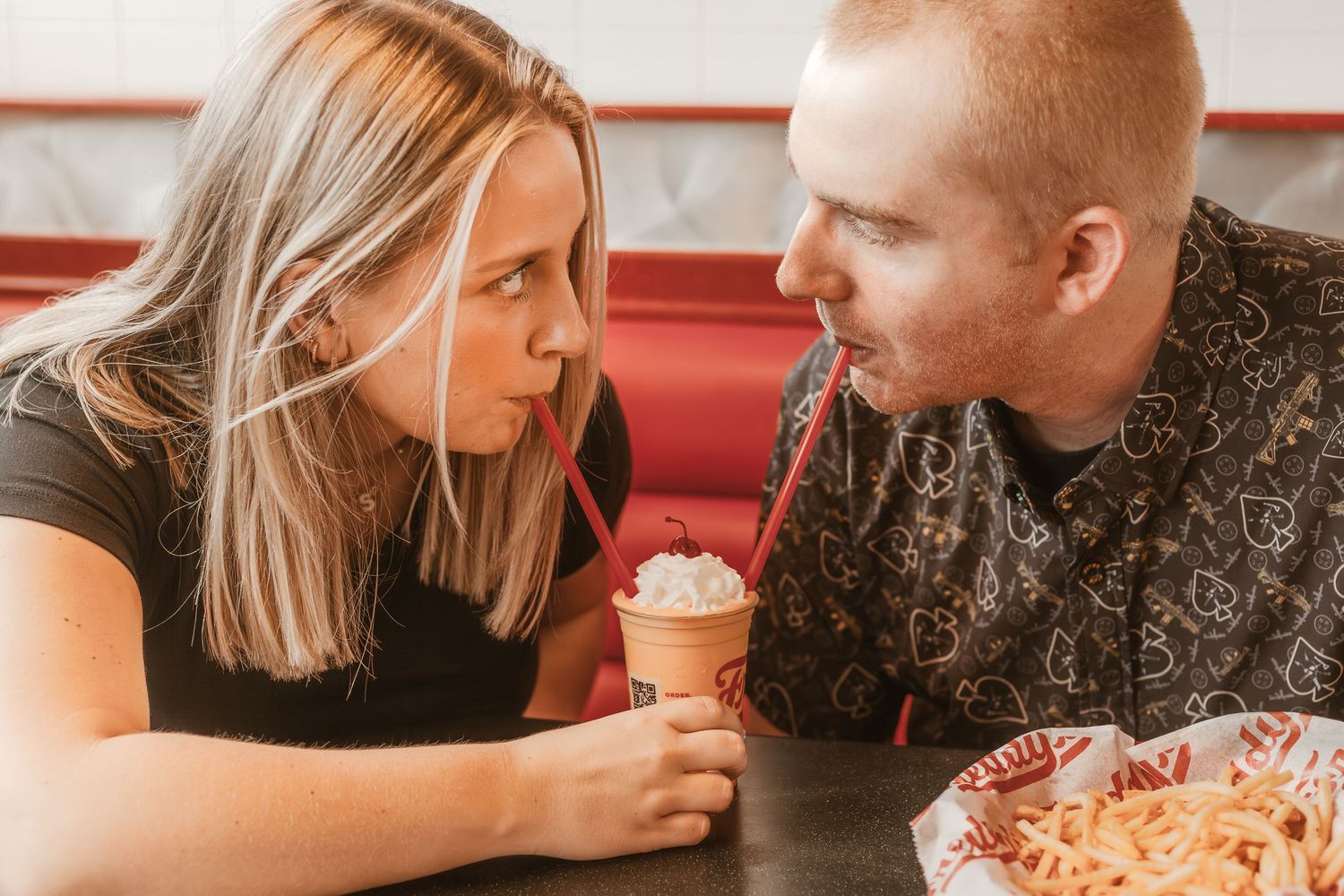 A couple shares dessert and pizza at a diner booth.
