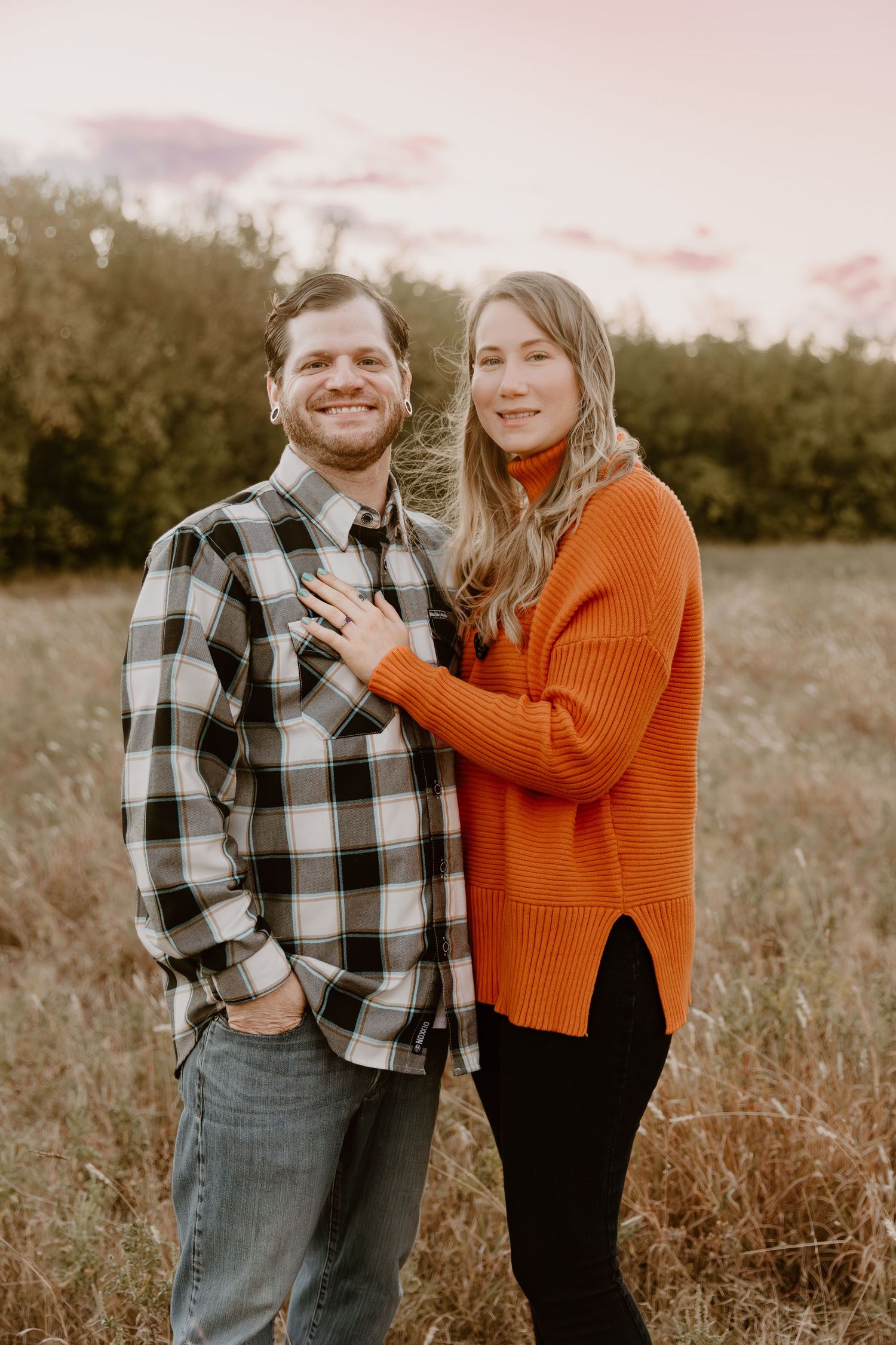 A couple shares a joyful moment together in a field wearing plaid and orange sweaters during golden hour.