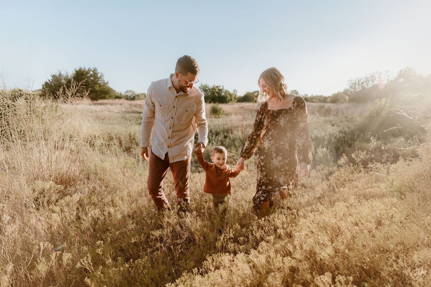 A couple walks through a sun-drenched meadow of tall golden grass during a warm summer evening.