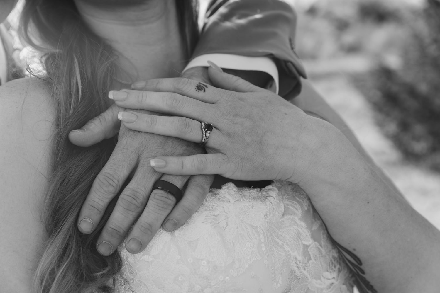 Black and white photo of a bride and groom embracing, showcasing their wedding rings on clasped hands.