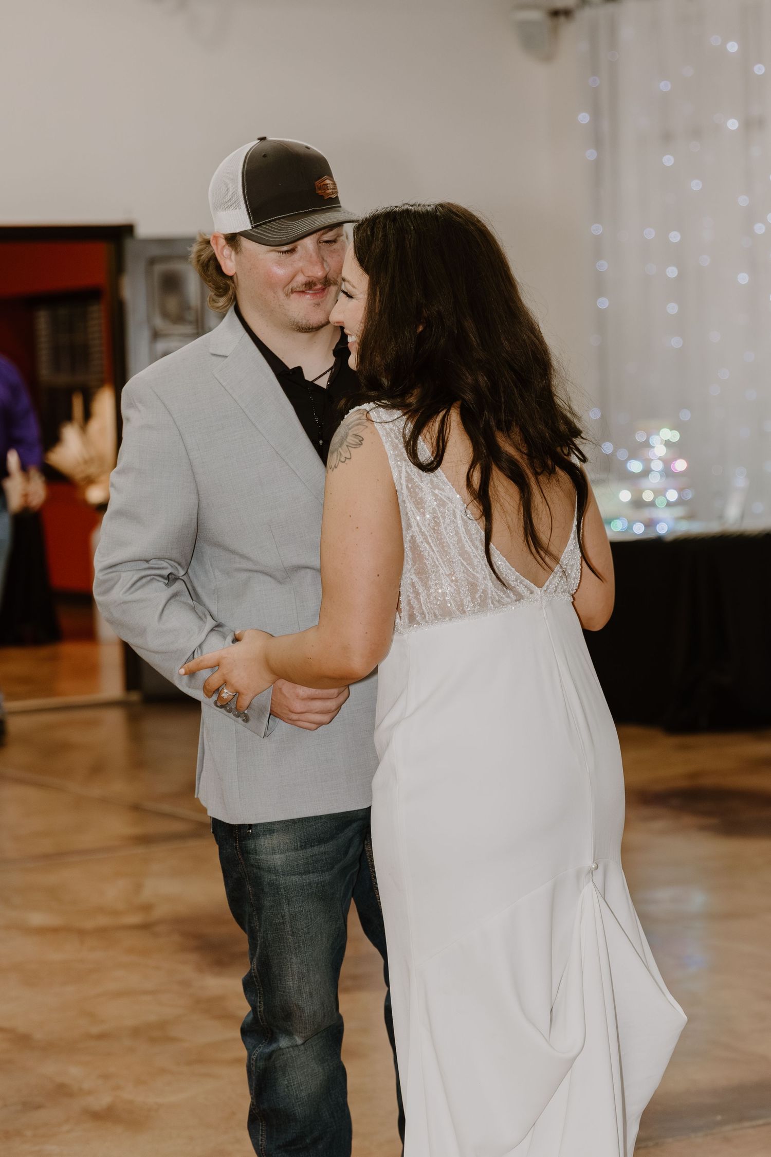A couple shares an intimate dance moment on a wooden floor with twinkle lights in the background.
