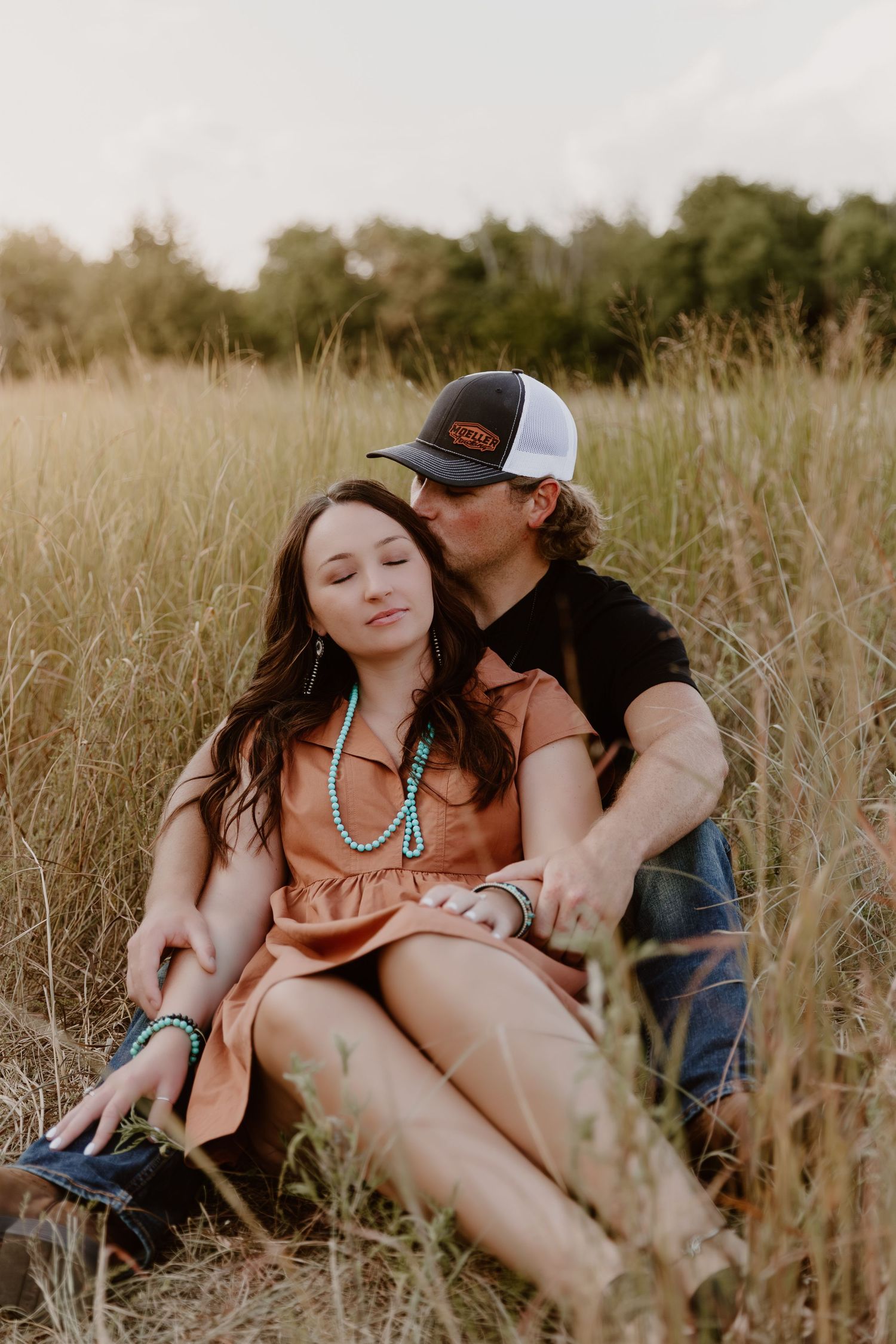 A couple shares an intimate moment while sitting together in a tall grass field during golden hour.