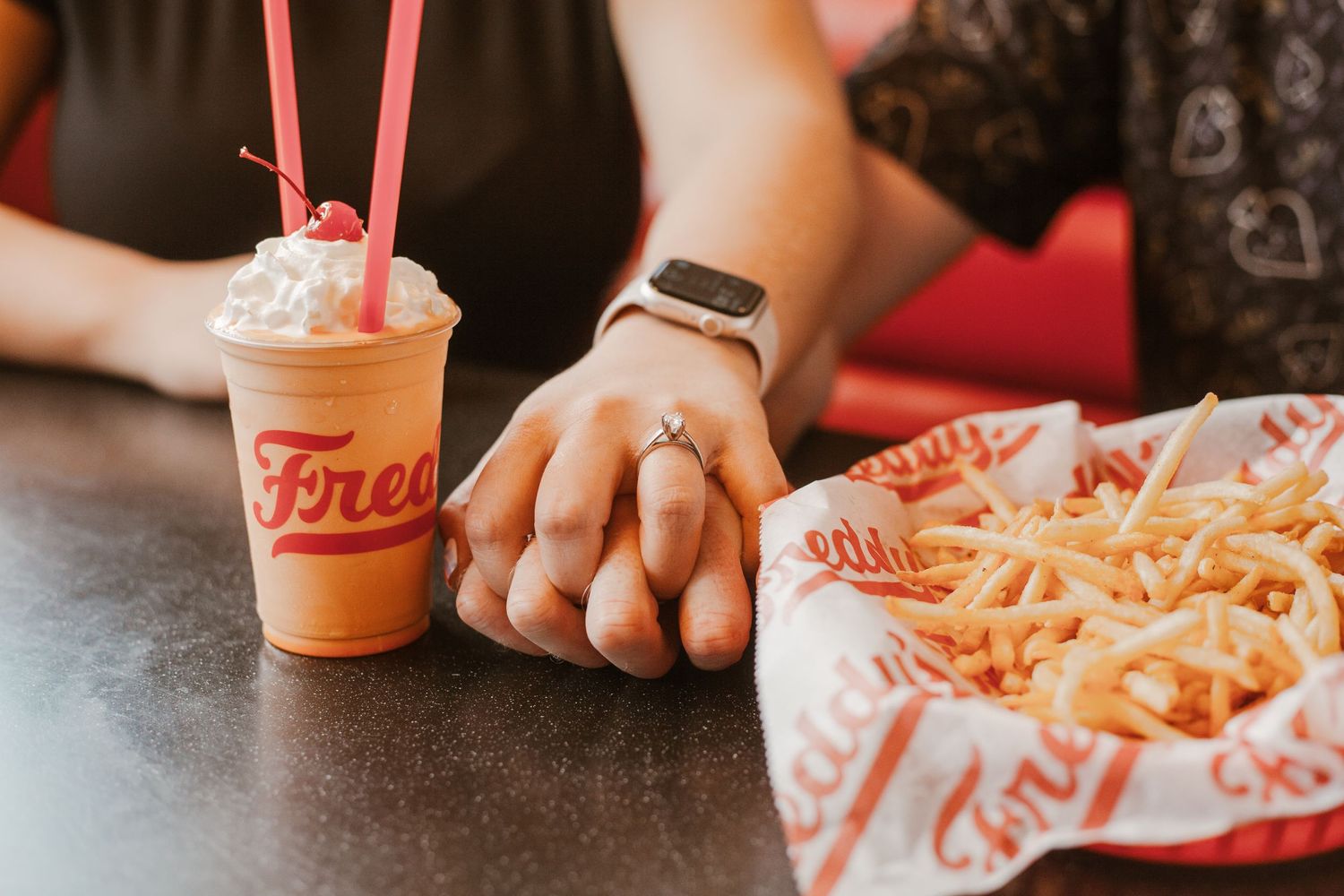 Close-up of hands holding milkshake with french fries at Freddy's restaurant.