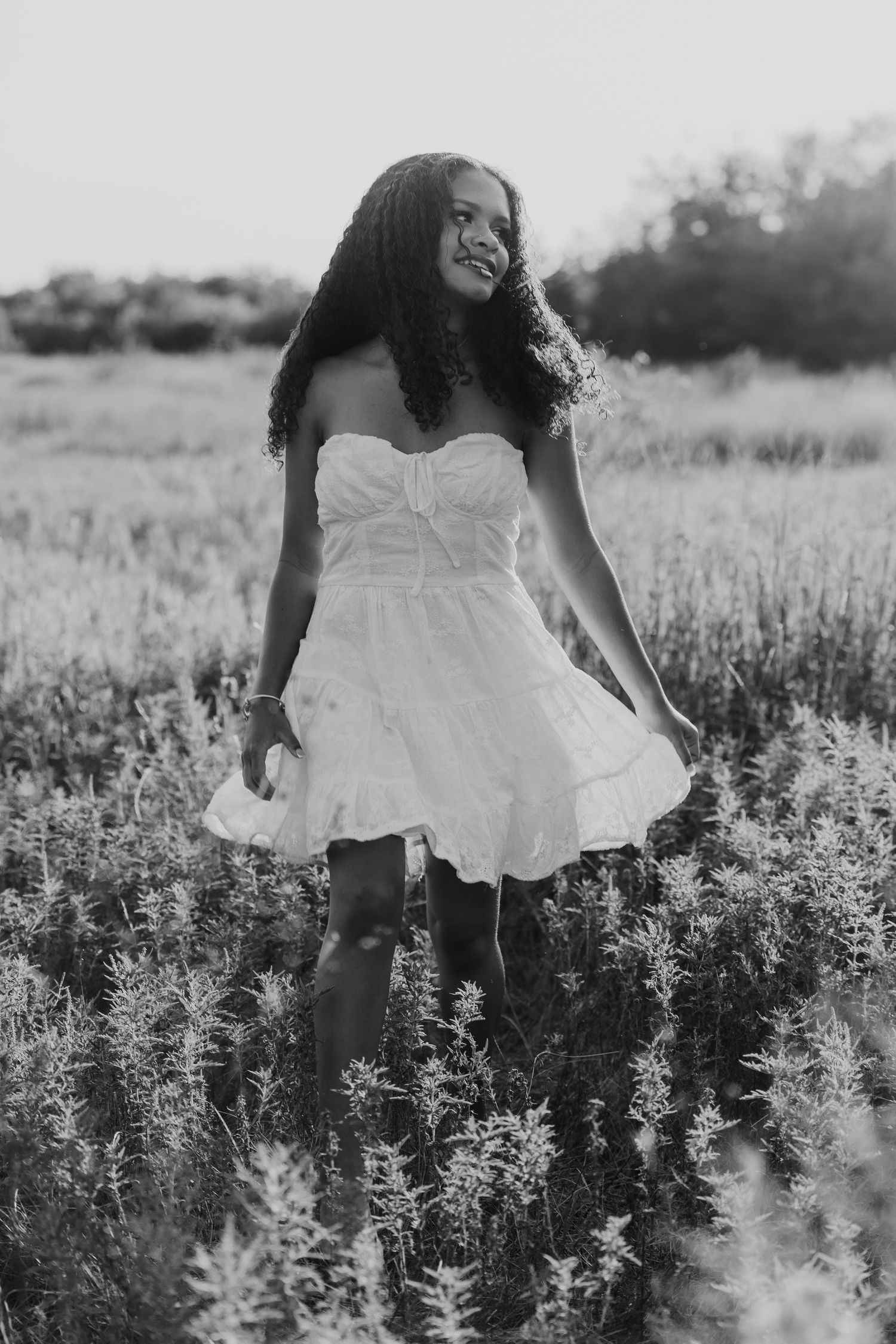 Black and white photo of someone in a white dress walking through a flowering meadow in summer.