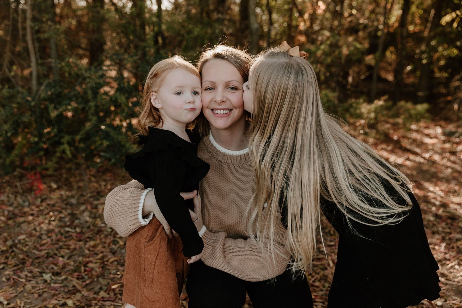 A family shares tender moments together in a wooded setting during golden hour.