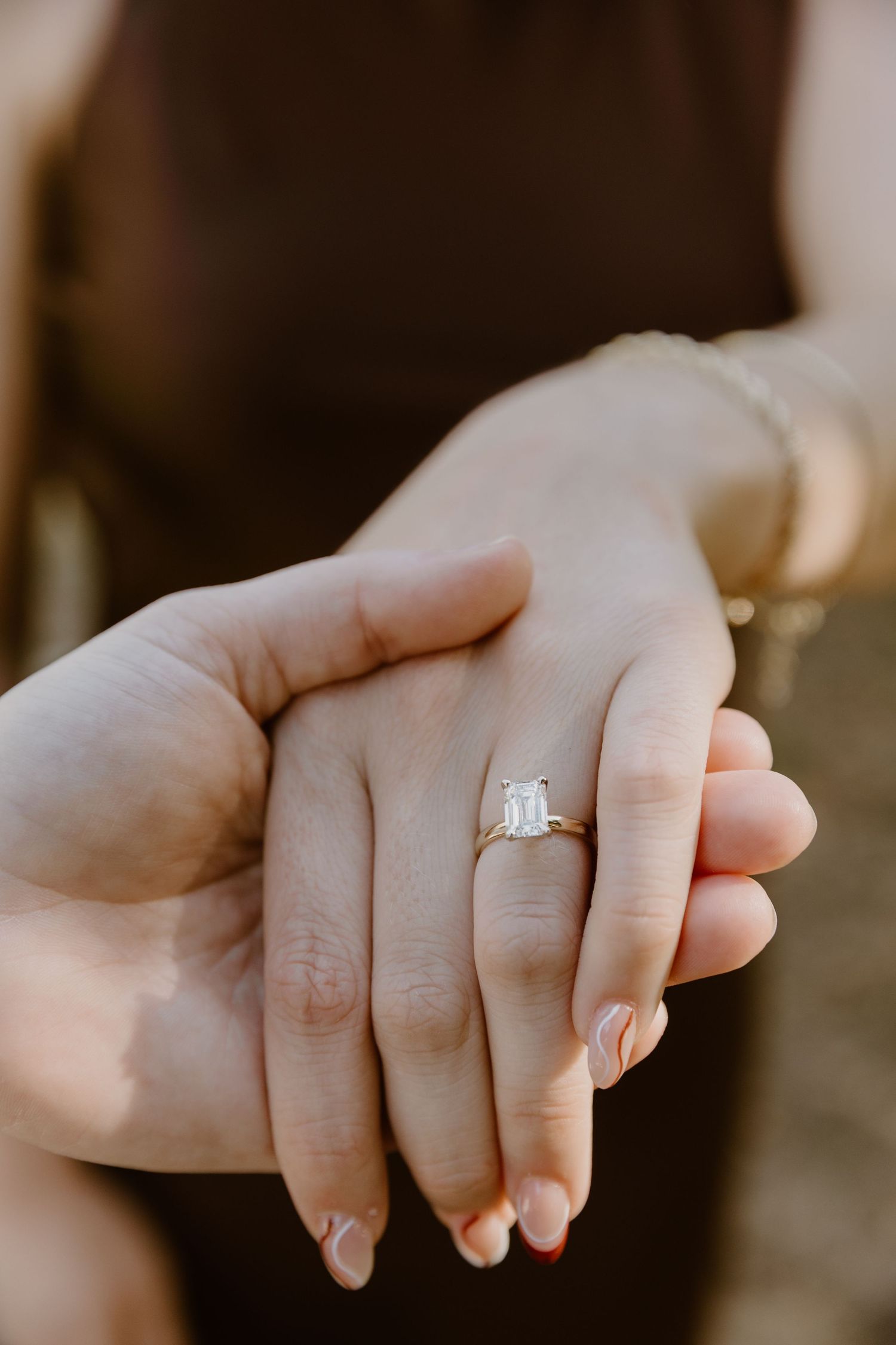 Close-up view of intertwined hands with a delicate silver ring in warm lighting.