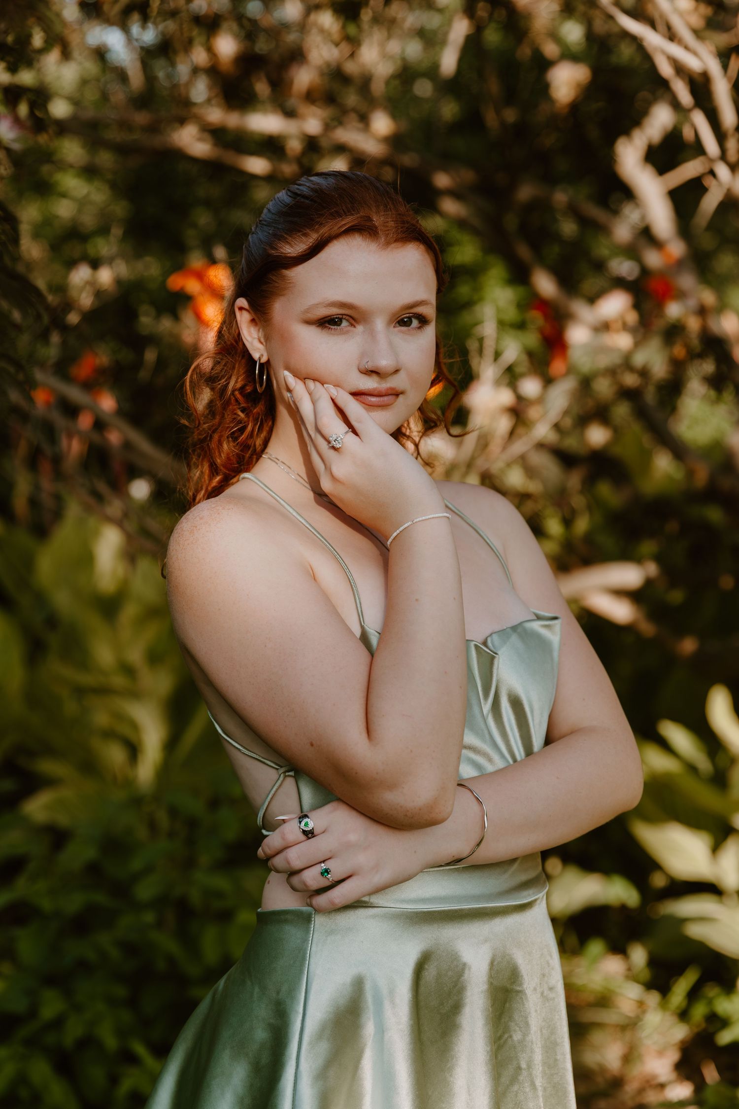 Portrait of someone in a mint green satin dress posing in a sunlit garden setting.