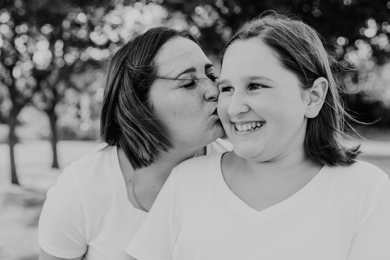 A sweet black and white portrait of a tender moment between two people in matching white shirts outdoors.