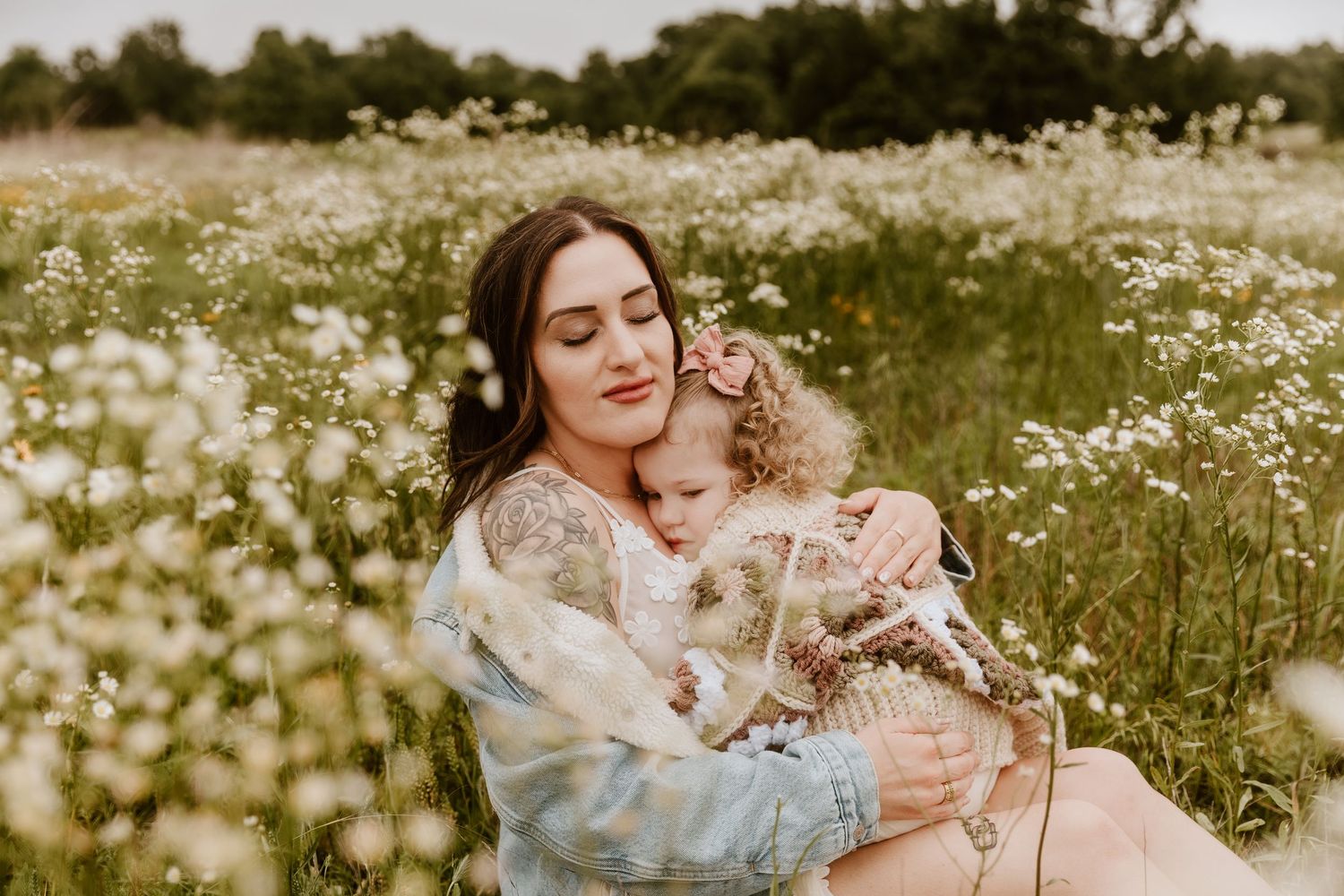 Mother holding young child in a field of white wildflowers, sharing a tender embrace outdoors.