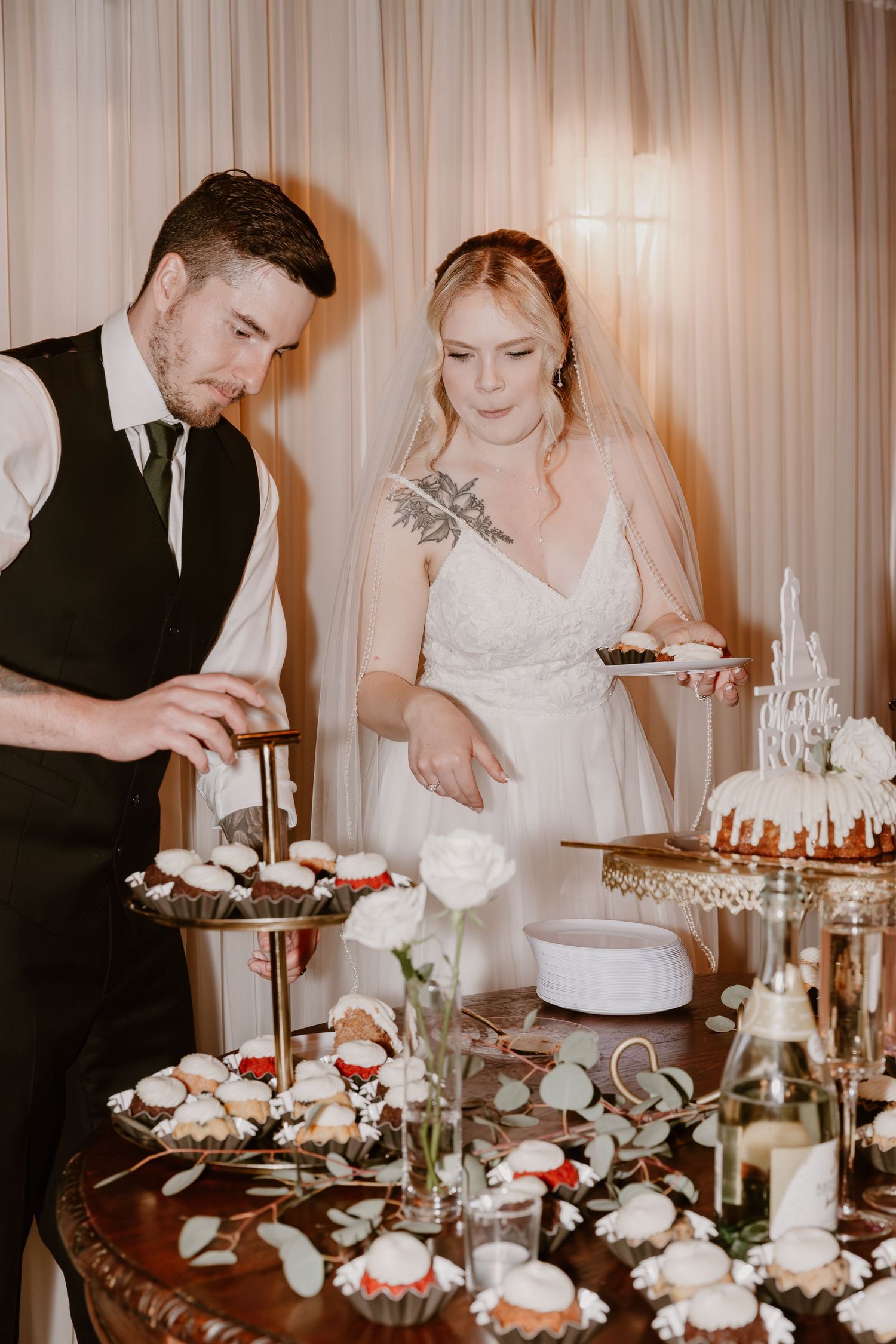 A couple cutting desserts at their wedding reception with an elegant display of sweets and treats on the table.
