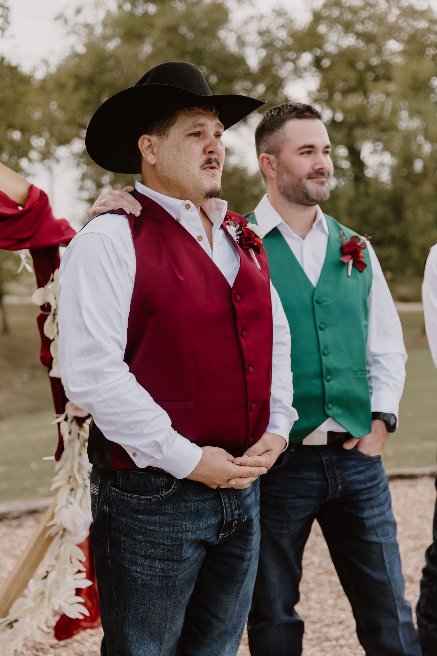 Groomsmen in western attire with burgundy and green vests stand together outdoors during a country wedding.