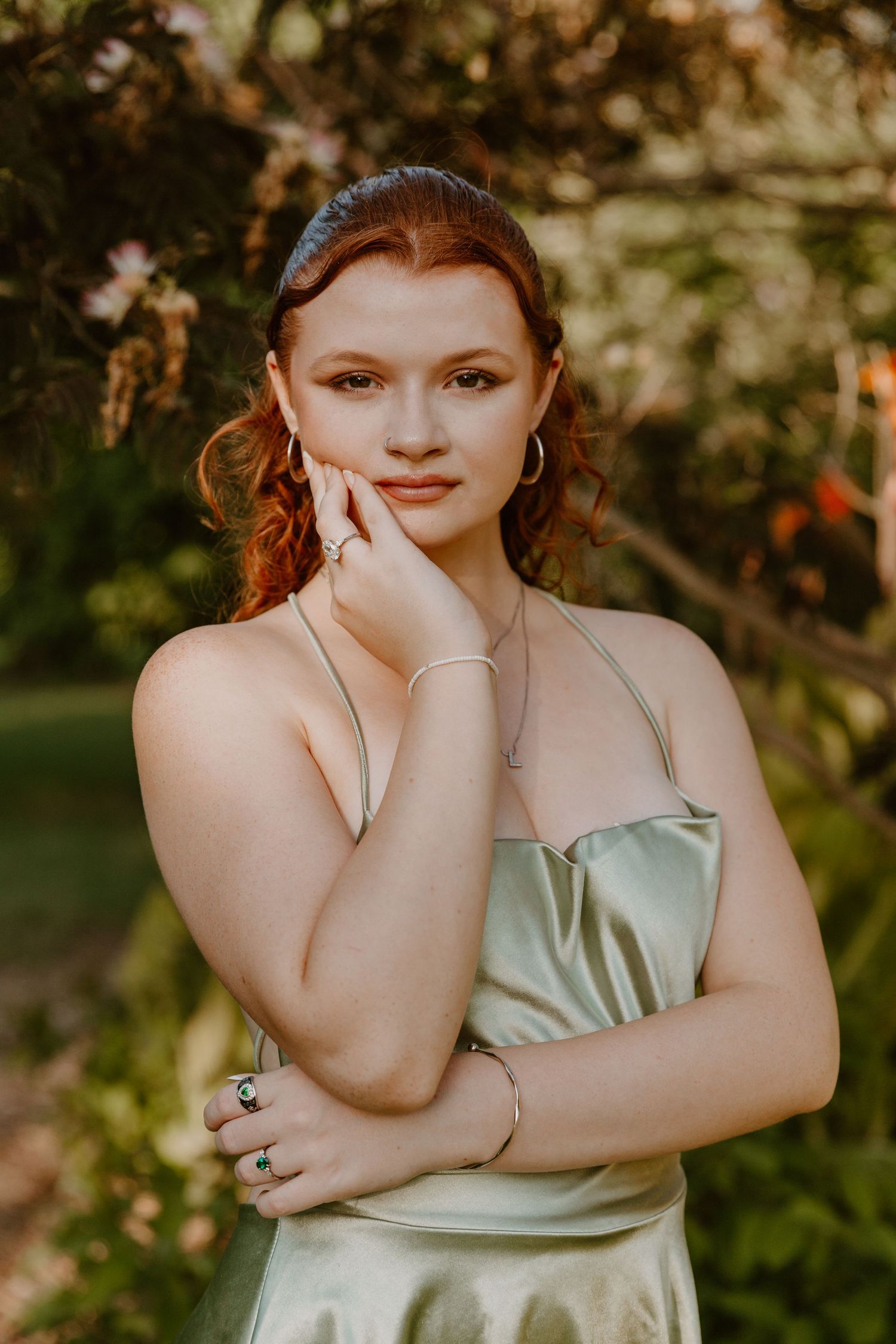A photoshoot in a garden setting features a model in a pale mint-colored satin dress posing gracefully against natural foliage.