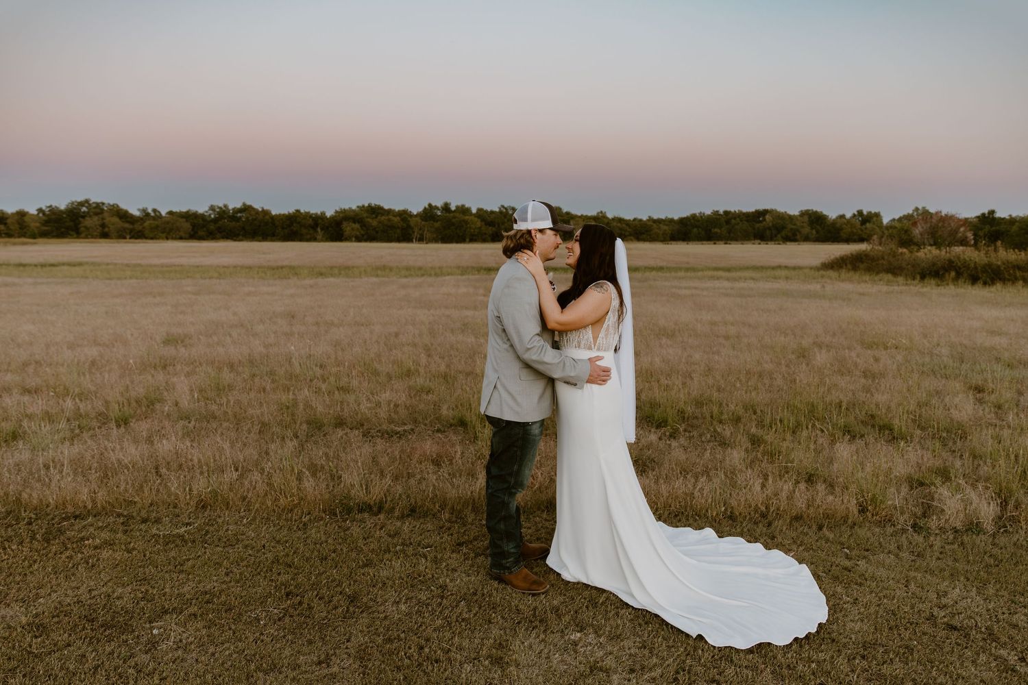 A romantic wedding scene in an open field with a couple embracing during golden hour.