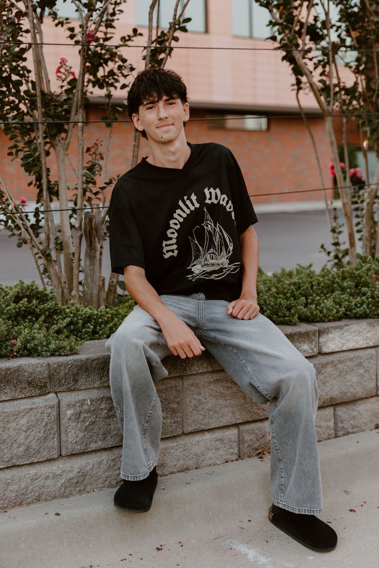 Close up shots of someone in casual attire sitting on a concrete ledge wearing jeans and a black t-shirt.