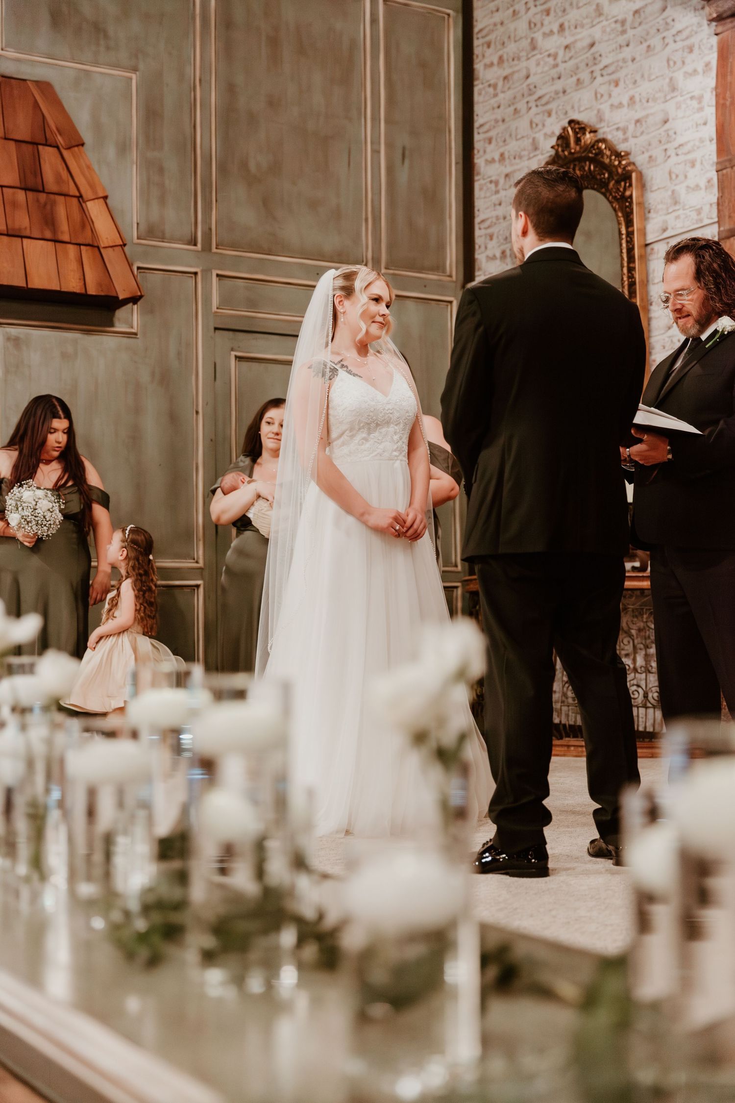 Wedding ceremony moments captured in an industrial brick venue with white floral decorations in the foreground.