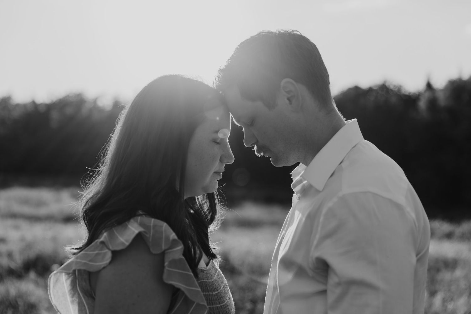 A couple embraces outdoors in a romantic silhouette against a natural setting during golden hour.