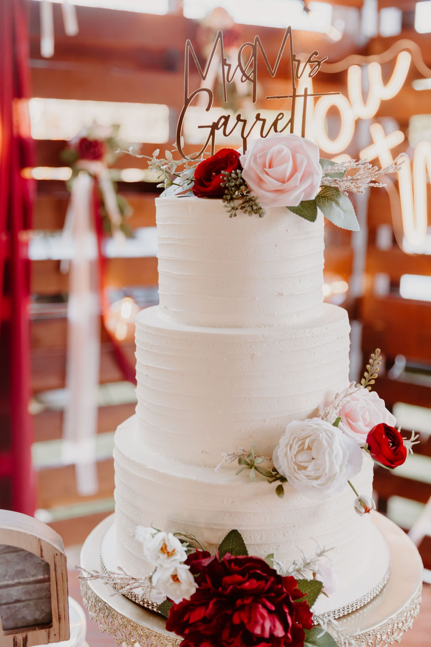 Elegant three-tier white wedding cake decorated with pink and burgundy roses on a silver stand.