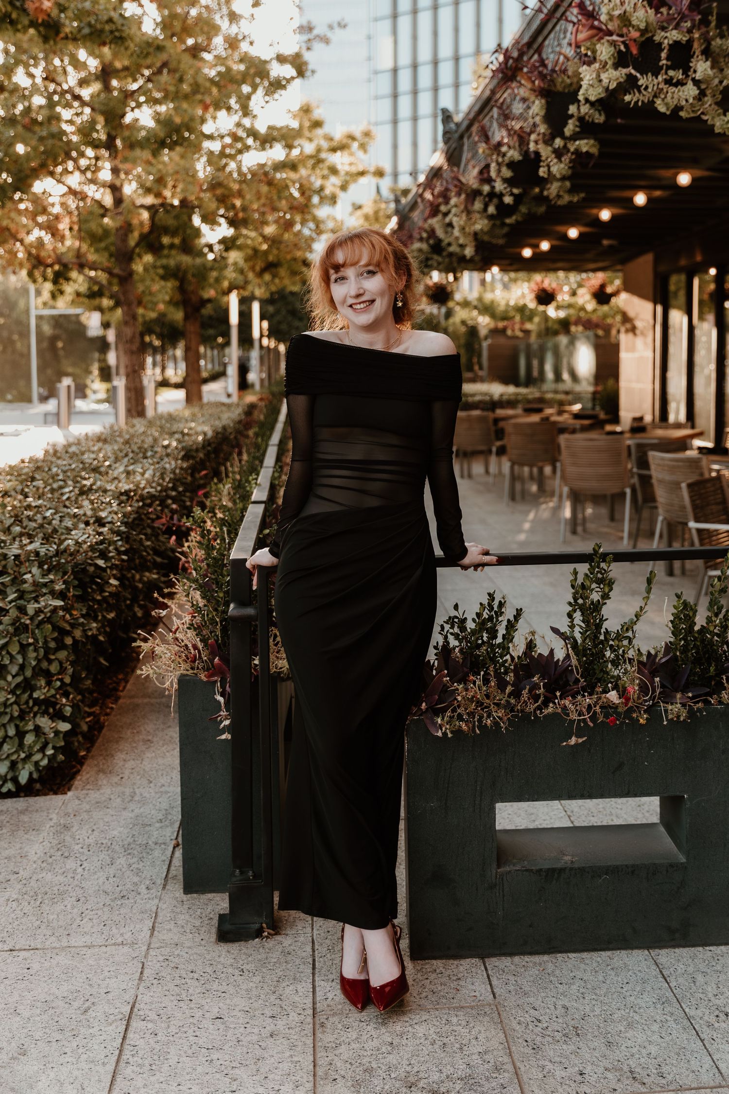 Black dresses and red shoes create an elegant contrast at an outdoor event with string lights and greenery.