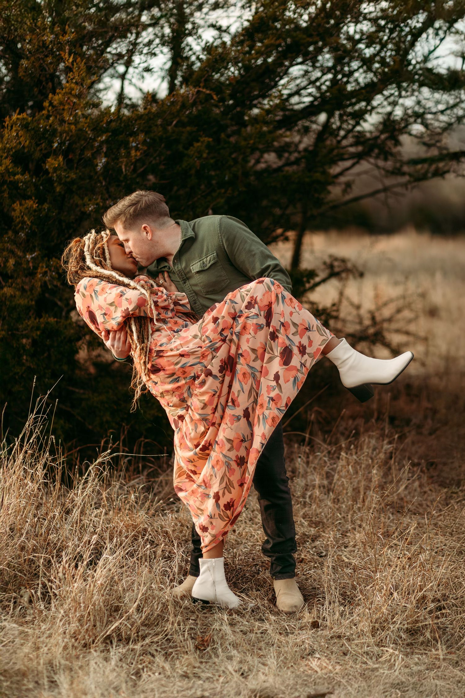 A romantic dip pose in a rustic field with flowing floral dress and casual attire.
