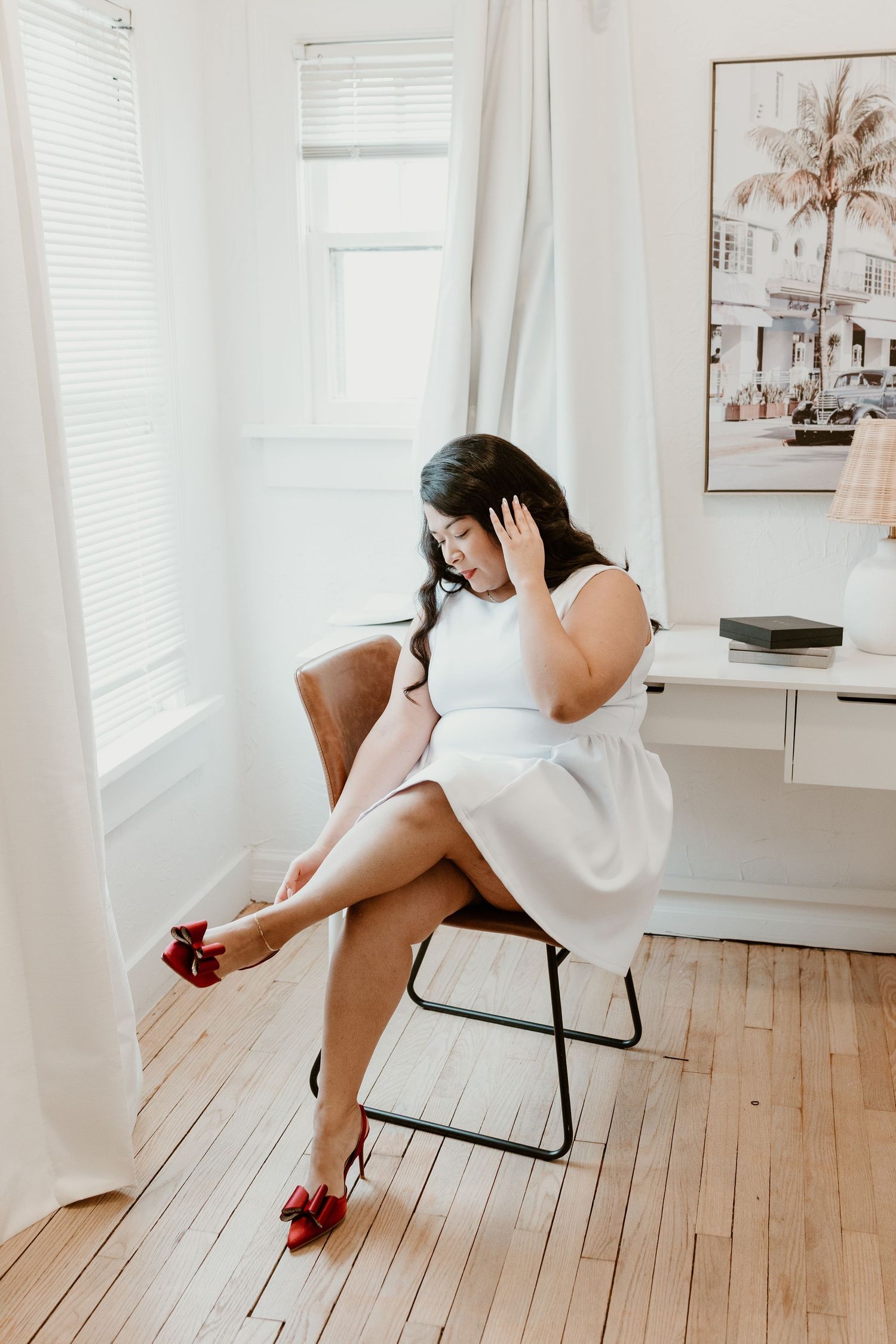 Person in white shirt reclines playfully across black chair on hardwood floor in bright minimalist room.