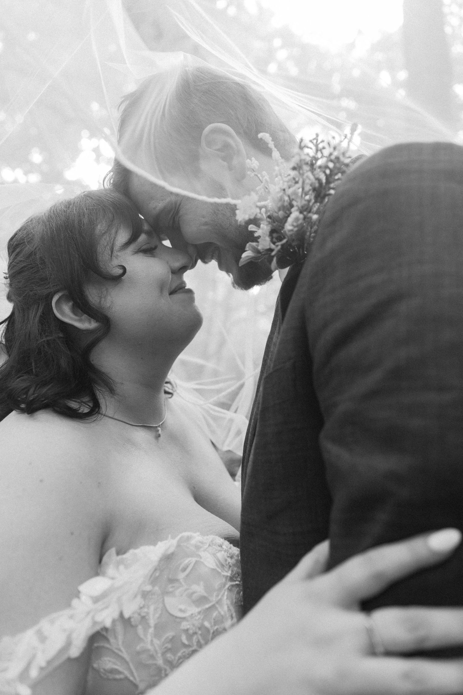Black and white close-up of bride and groom touching foreheads tenderly under veil, sharing intimate wedding moment.
