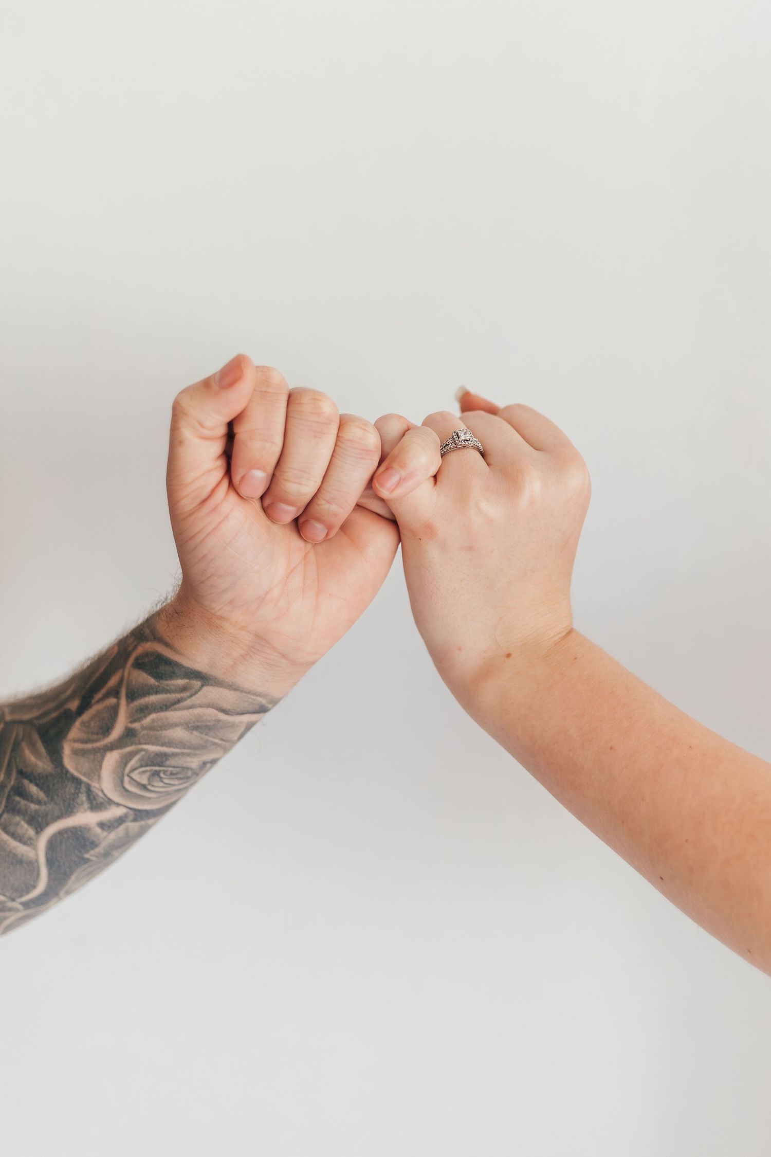 Close-up of pinky promise between two hands, one with sleeve tattoo.