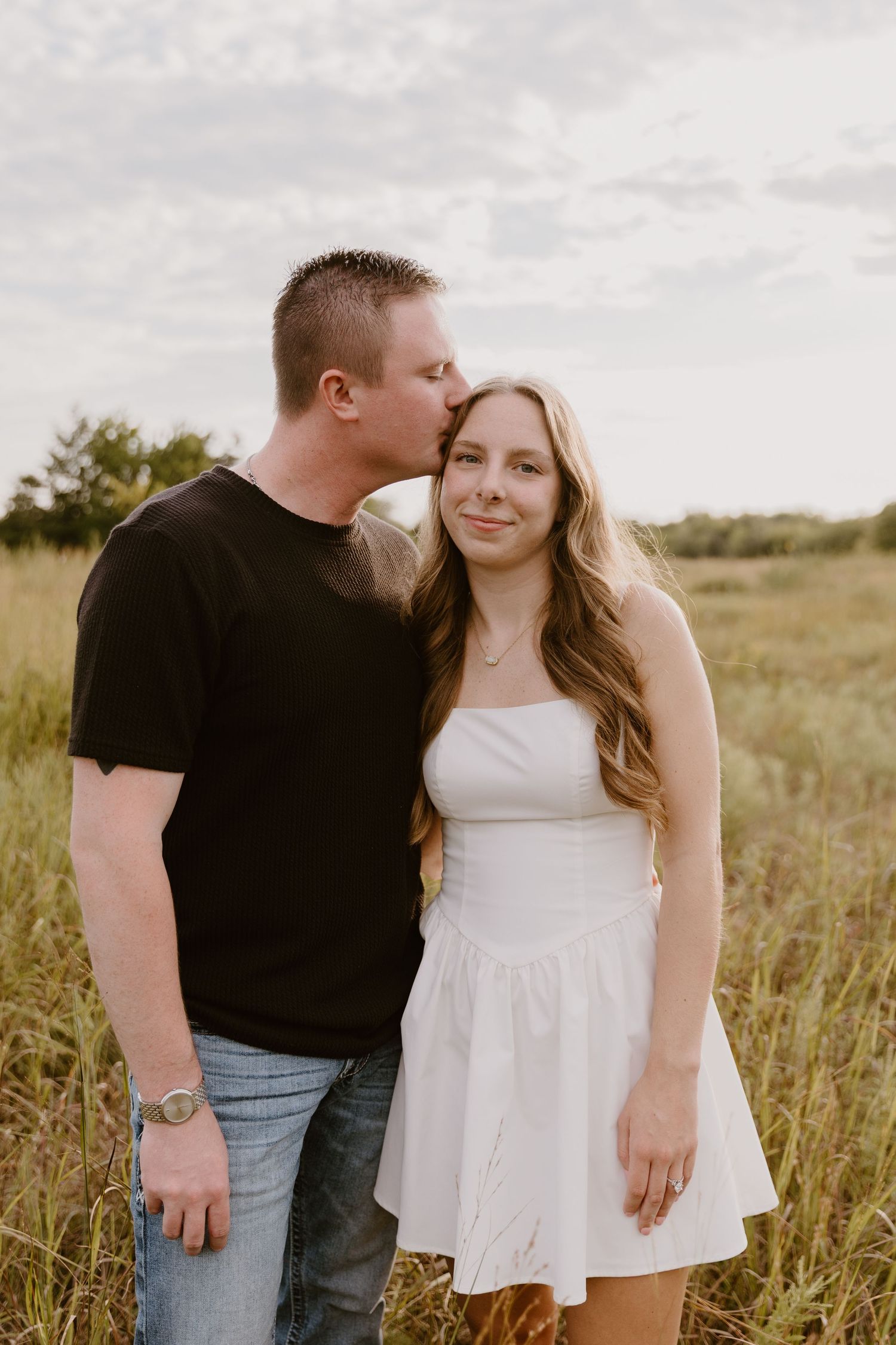 A couple shares an intimate moment in a sunlit field of tall grass during a summer engagement photoshoot.