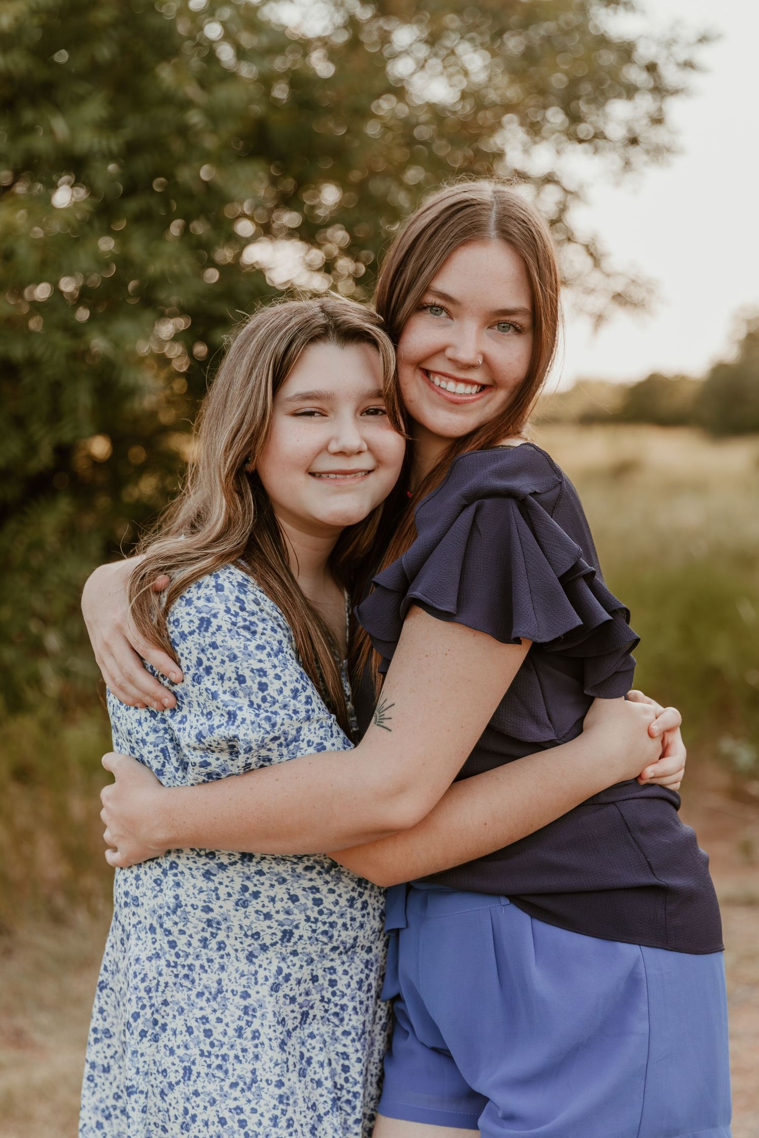 Two people embrace and smile while posing outdoors in casual summer attire during golden hour lighting.