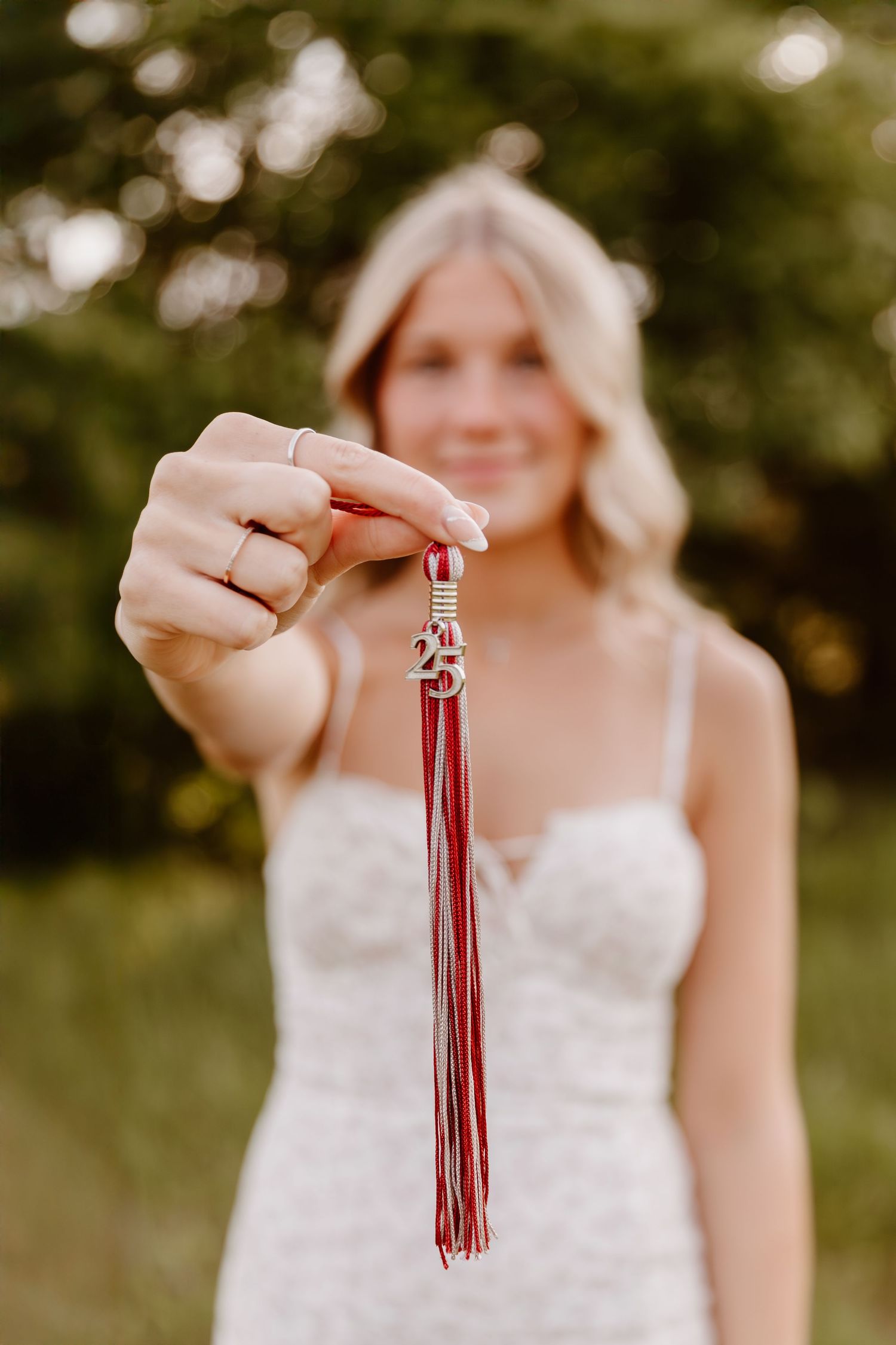 A close-up shot of hands holding a red graduation tassel against a blurred outdoor background.