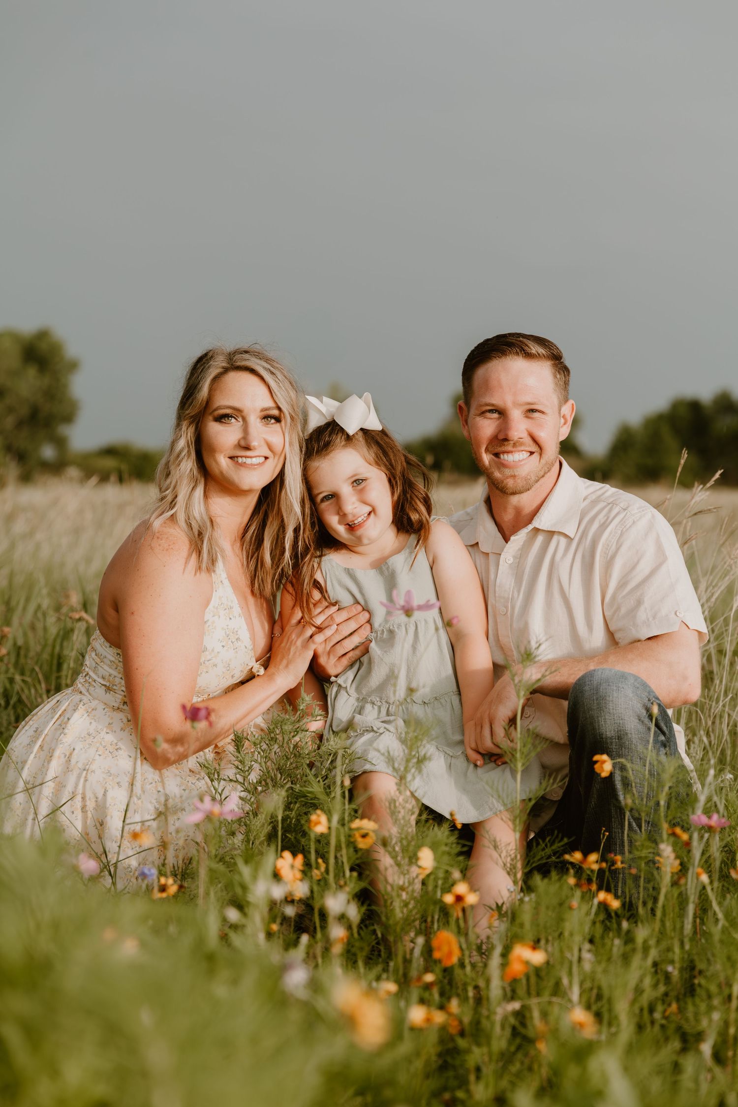 A family laughs together while sitting in a sunny wildflower meadow wearing coordinated white and cream outfits.