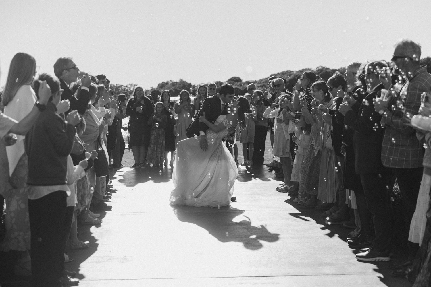 Person in white robe kneeling on path lined with crowd of onlookers in black and white photo.