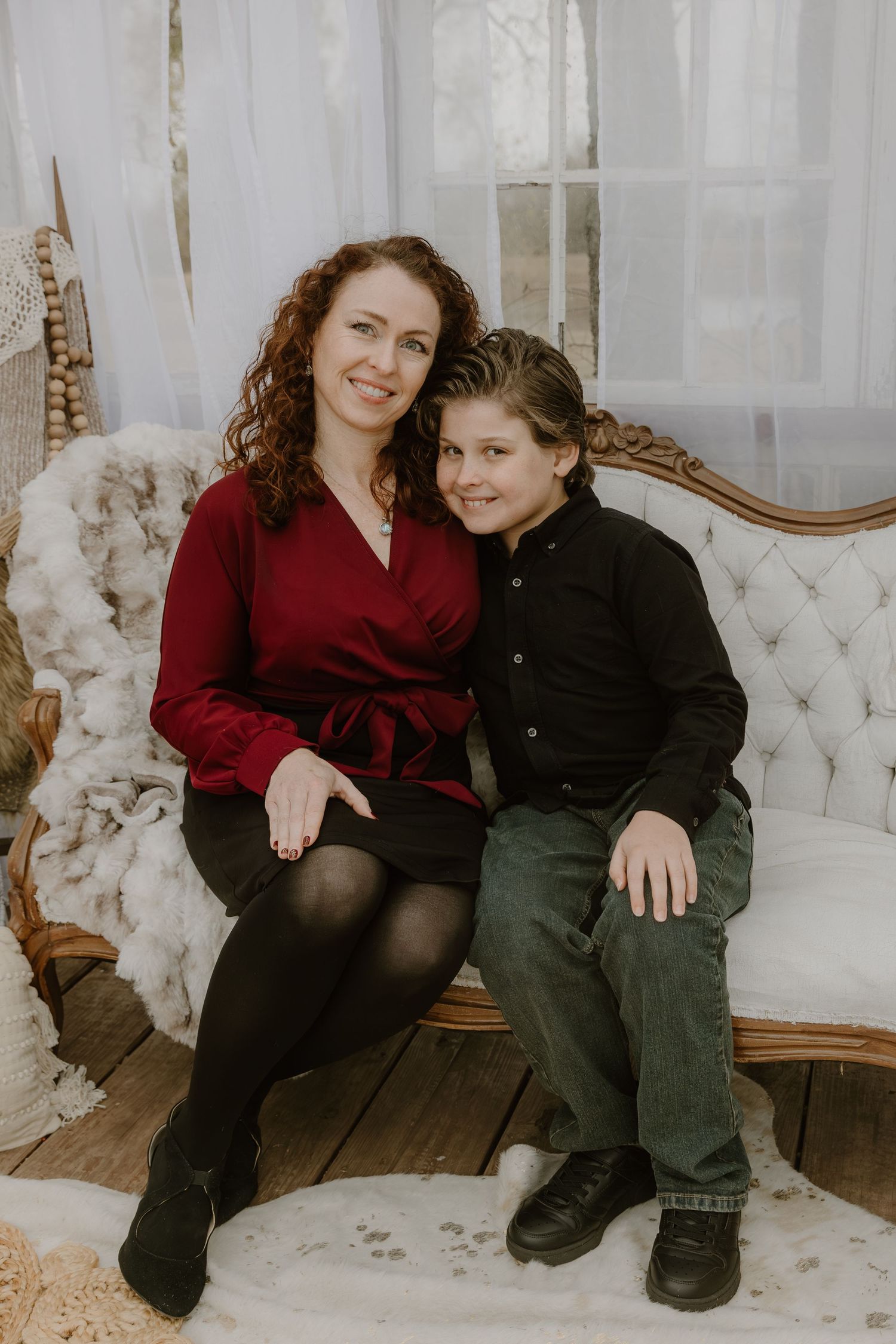 Two people in contrasting red and black outfits share tender moments while sitting on an elegant white tufted sofa.