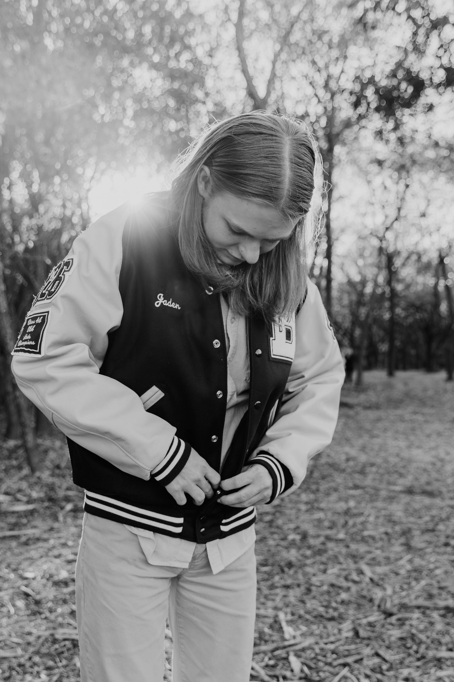 Black and white photo of someone wearing a varsity letterman jacket outdoors on a sunny autumn day.